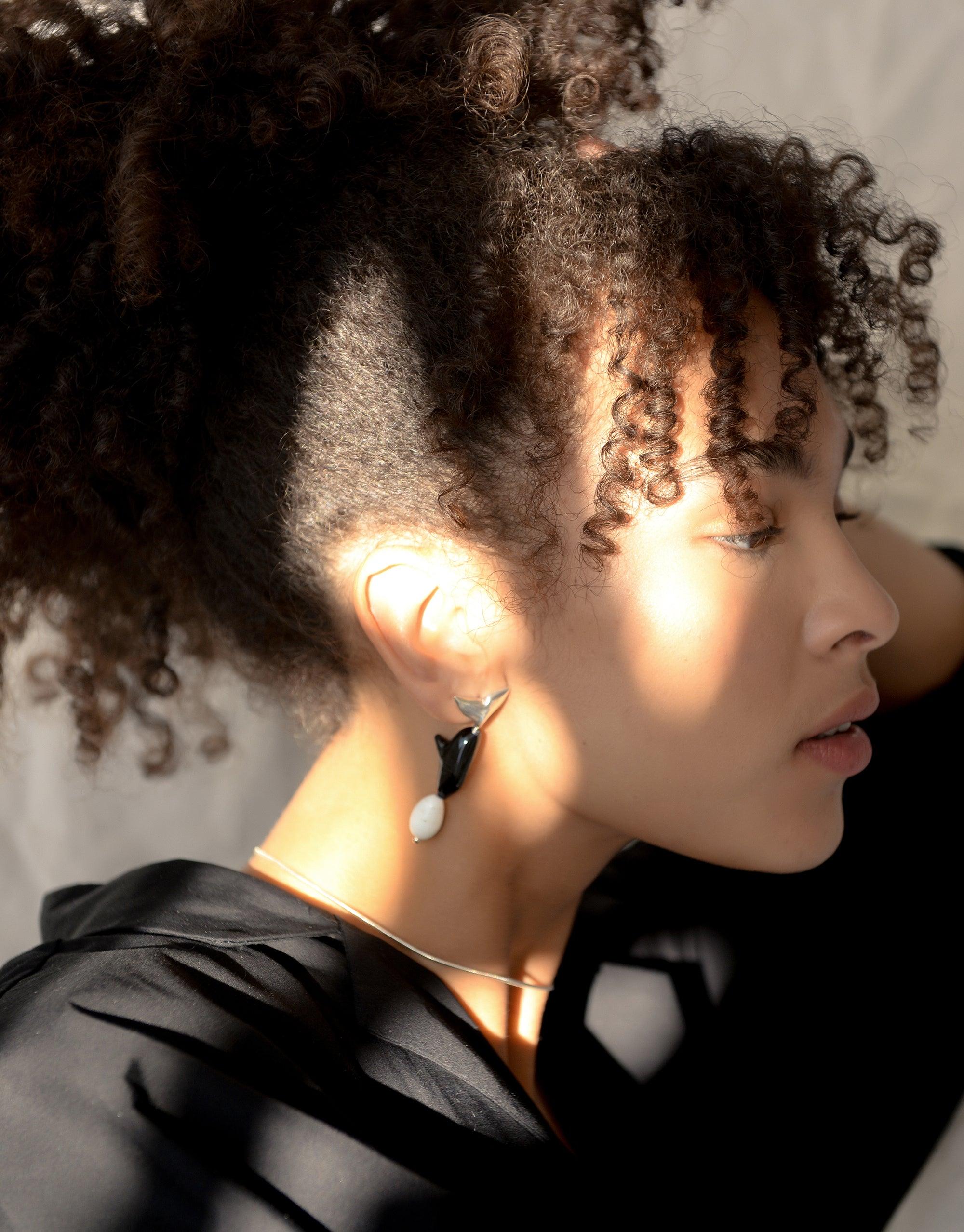 Side profile of a person with curly hair wearing Orca Earrings, featuring a black and white design inspired by marine mammals. Eco-friendly jewelry made from repurposed glass, showcasing sustainable fashion and climate change awareness. CLED, Orca Earrings.