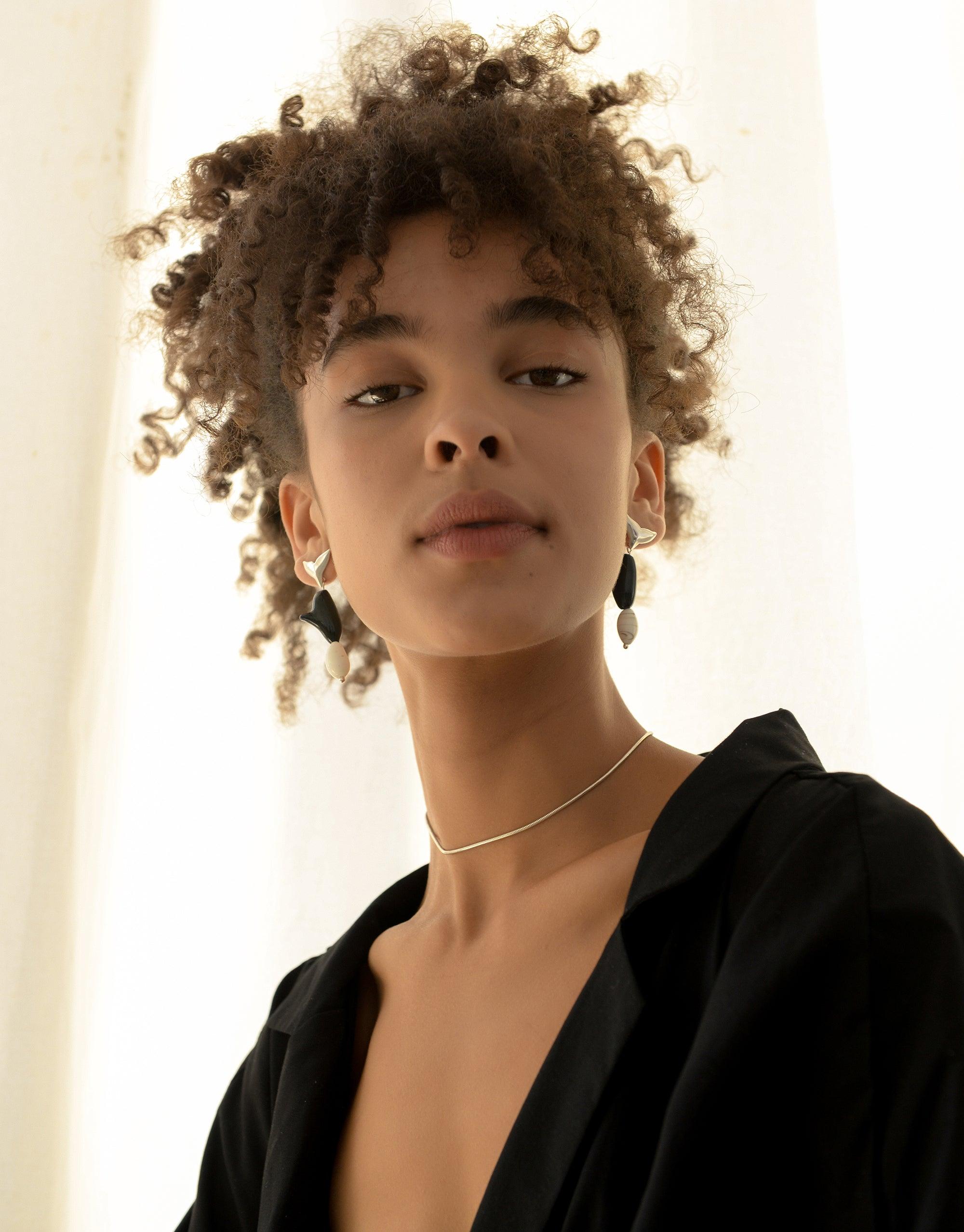 Elegant model wearing Orca Earrings from the Floating Glacier Collection, showcasing eco-friendly jewelry made from repurposed glass. Stylish black and white design highlights the earrings' unique shape inspired by marine life. Sustainable fashion statement by CLED.