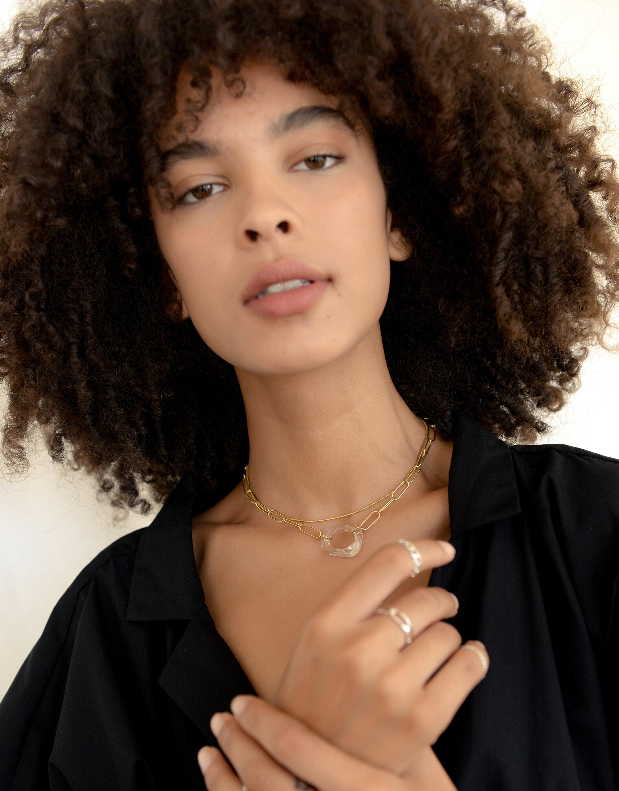 The Day Loop Necklace elegantly displayed on a woman with curly hair, showcasing its minimal oval chain design, crafted from eco-friendly repurposed glass, embodying CLED's sustainable jewelry ethos.