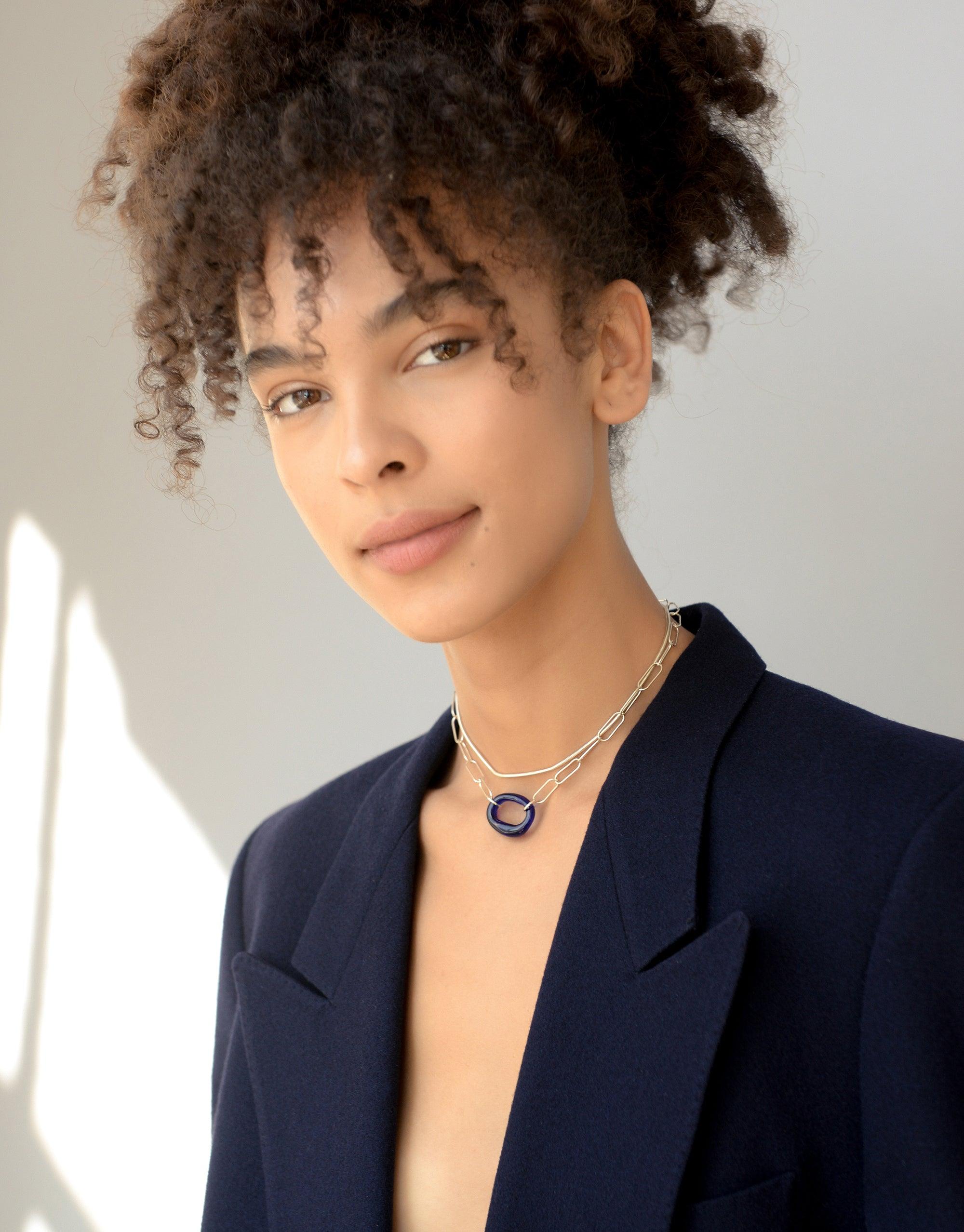 The Day Loop Necklace elegantly adorns a woman's neck, showcasing an oval chain design. This minimal piece is crafted with repurposed Eco Gems, embodying CLED's eco-conscious ethos.