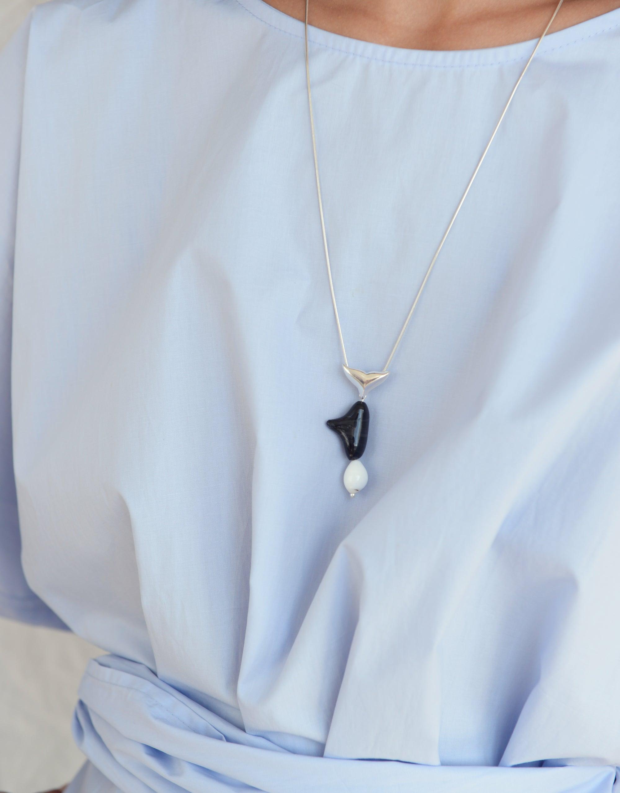 Orca Necklace featuring a stylized black orca tail pendant with a white pearl accent, suspended on a delicate silver chain. Eco-friendly jewelry inspired by Arctic marine life and climate change awareness. Handcrafted from repurposed glass by CLED.