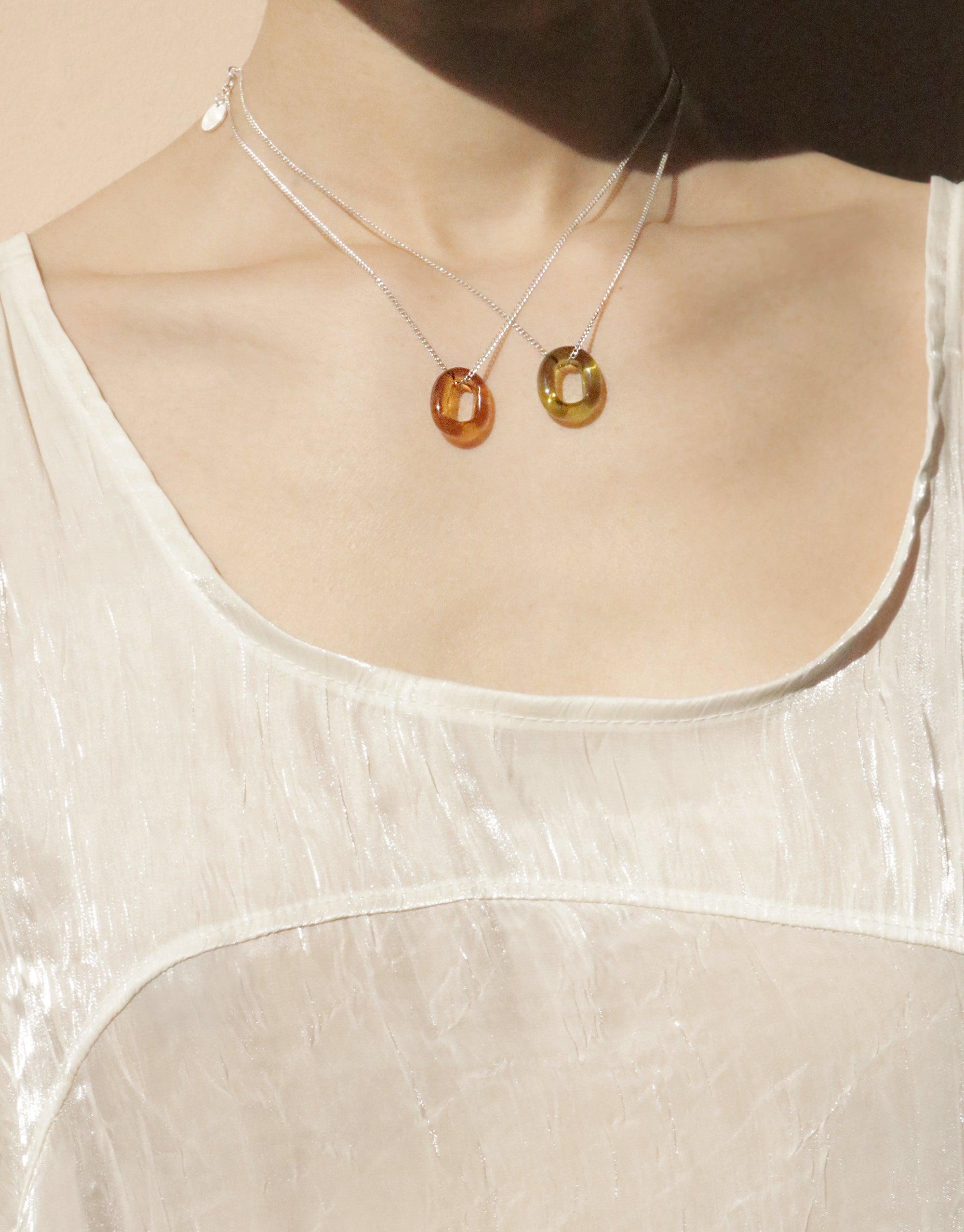 Elegant In The Loop Necklace featuring handmade eco glass pendants in amber and green hues, suspended on delicate silver chains. Minimalist design showcasing sustainable jewelry craftsmanship. Perfect for layering or wearing solo. CLED