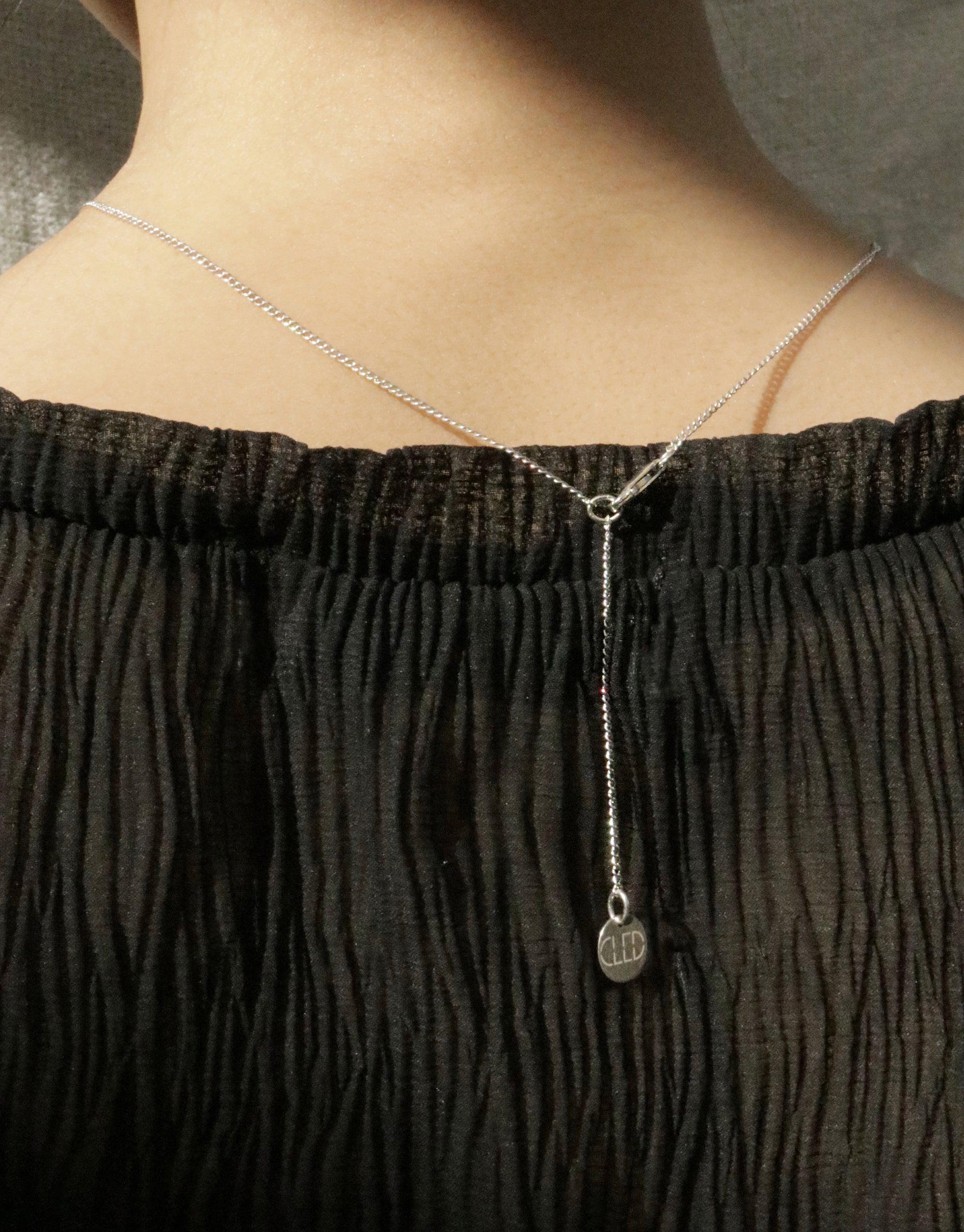 Close-up of a delicate silver chain necklace with a small loop pendant resting on a person's collarbone. The necklace contrasts beautifully against a black textured top. In The Loop Necklace by CLED showcases minimal elegance.