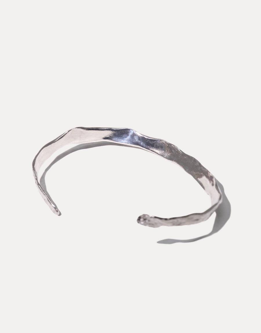Handcrafted sterling silver Cliff Bracelet with organic, curved design on white background. Open-ended cuff style with textured surface reflecting light. Minimalist and versatile accessory for everyday wear. CLED