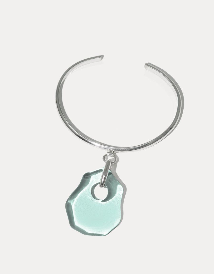 Elegant sterling silver cuff bracelet with a unique, aqua-colored eco-friendly glass pendant. The Coastline Drop Bracelet features a handcrafted, irregular-shaped charm inspired by sea glass, showcasing sustainable luxury and coastal aesthetics. CLED