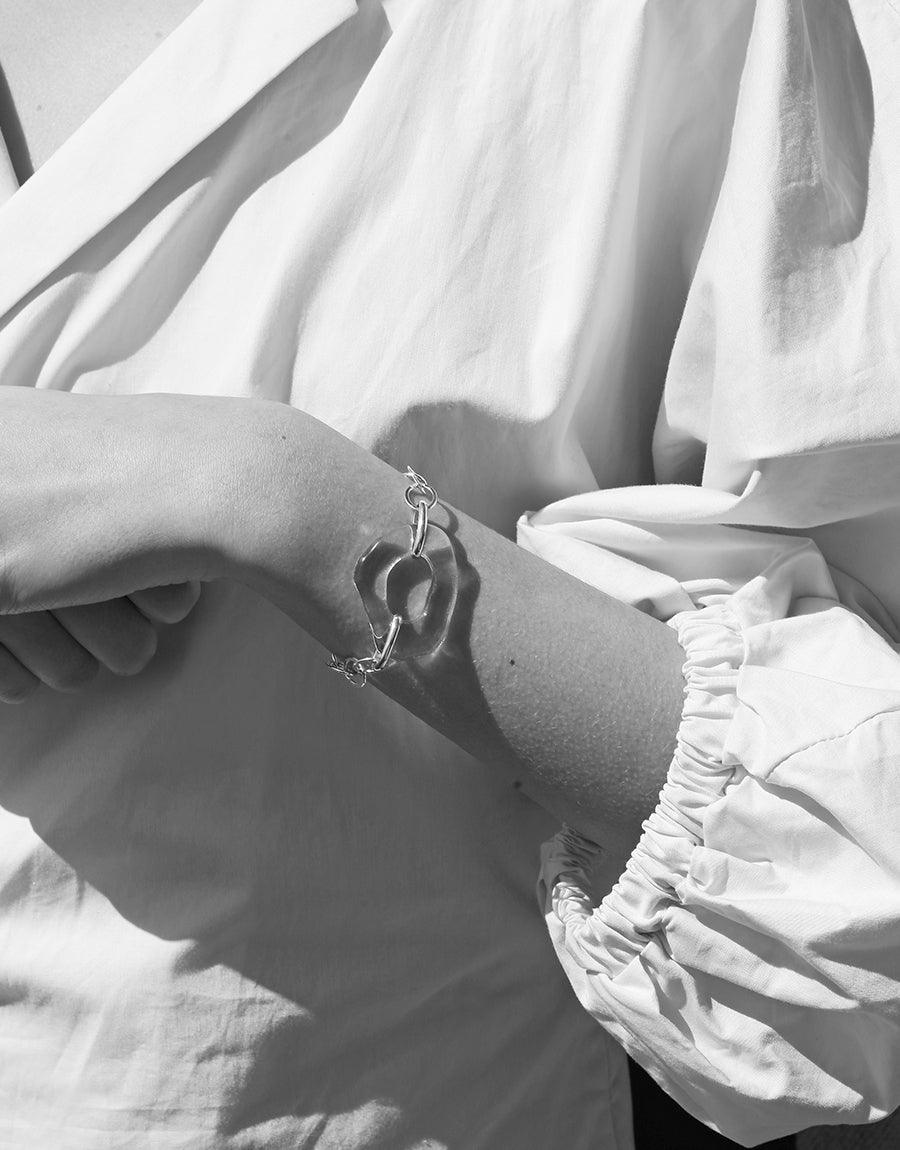 Elegant High Tide Oval Chain Bracelet in sterling silver, featuring a unique organic shape and repurposed glass Eco Gem. Shown on a model's wrist against flowing white fabric, highlighting its statement design and sustainable craftsmanship. CLED