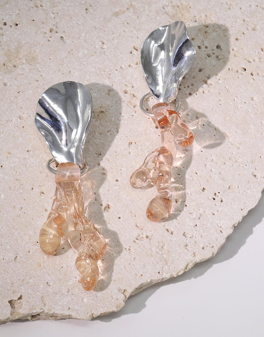 Coral Reef Earrings featuring silver-toned coral-shaped studs with dangling translucent glass elements, displayed on a textured beige surface. Handcrafted statement jewelry inspired by marine ecosystems. Sustainable design by CLED.