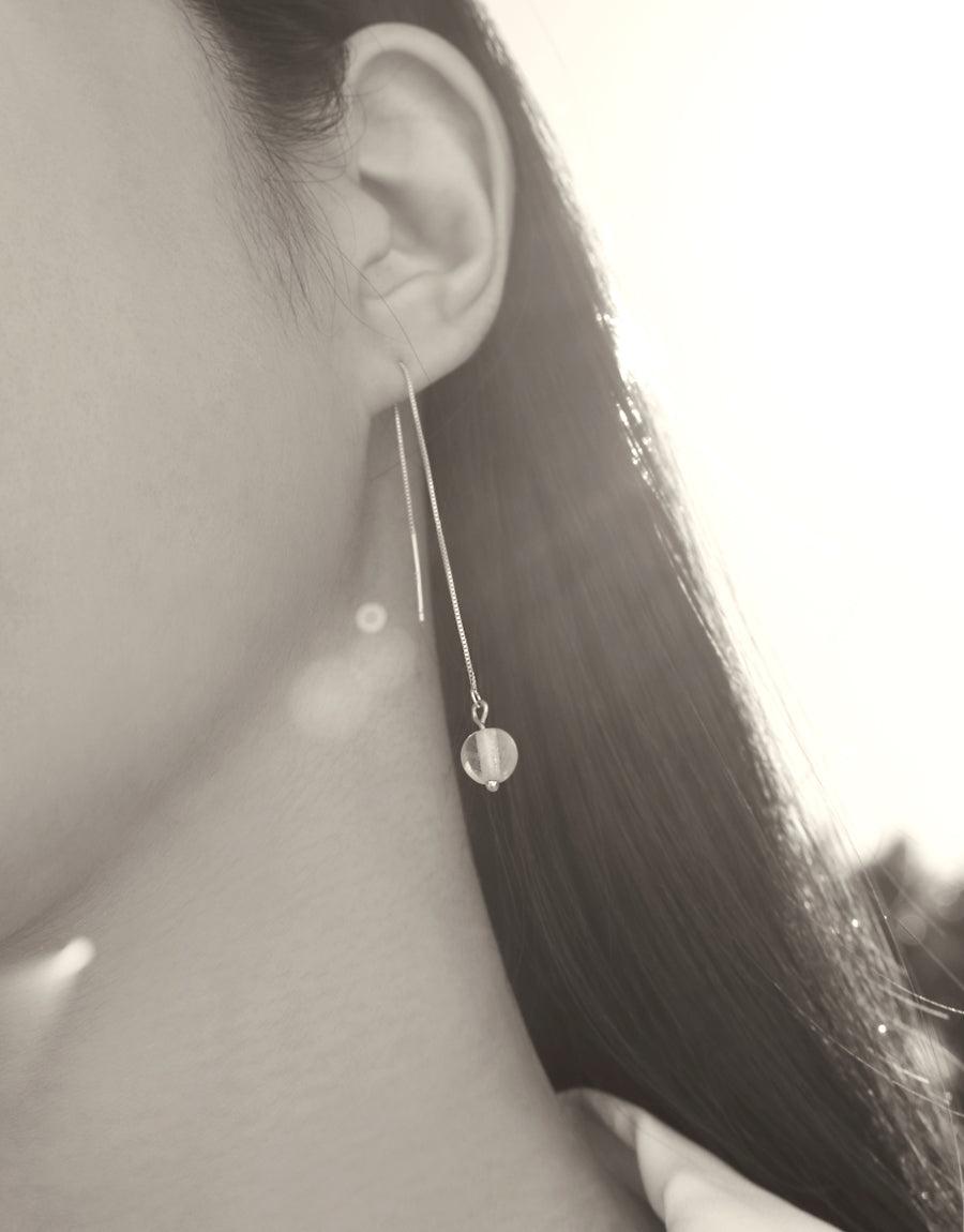 Close-up of a person wearing Minimal Line Earrings, featuring a delicate sterling silver chain with a small glass Eco Gem pendant. The earring hangs elegantly from the ear, showcasing its minimalist design and eco-friendly craftsmanship. Handmade by CLED.