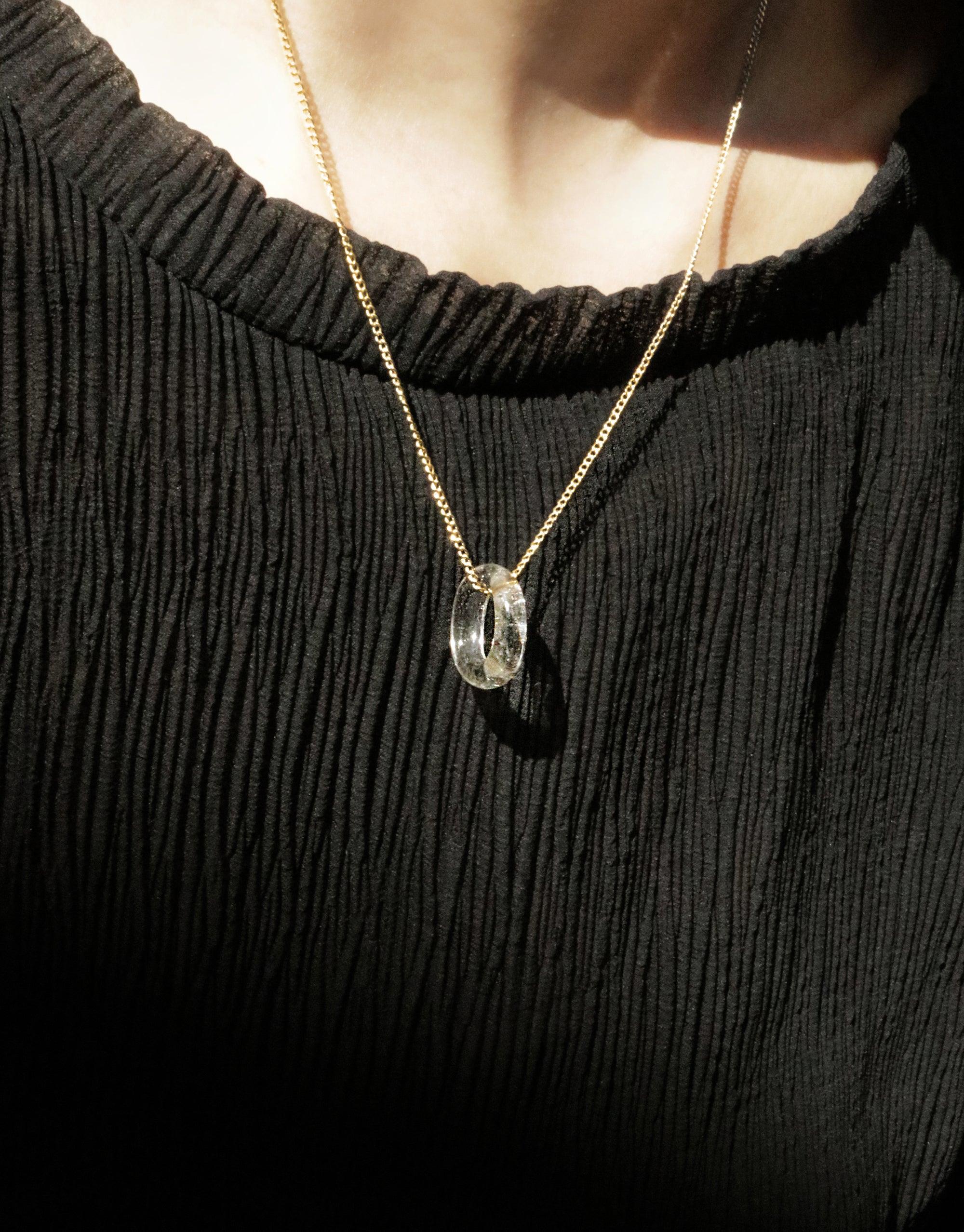 Elegant In The Loop Necklace featuring a delicate clear glass eco gem pendant on a gold chain, worn against a black ribbed sweater. Minimalist and sustainable jewelry design by CLED.