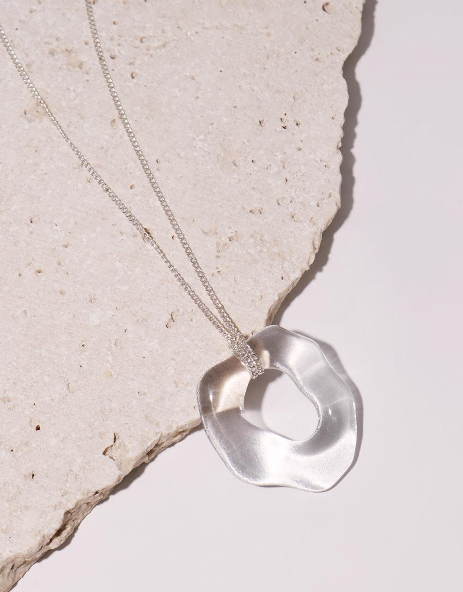 High Tide Necklace featuring a unique, organically shaped clear glass pendant on a delicate silver chain. Eco-friendly jewelry made from repurposed glass bottles, showcasing sustainable craftsmanship. Elegant and minimalist design perfect for ocean lovers. CLED High Tide Necklace.