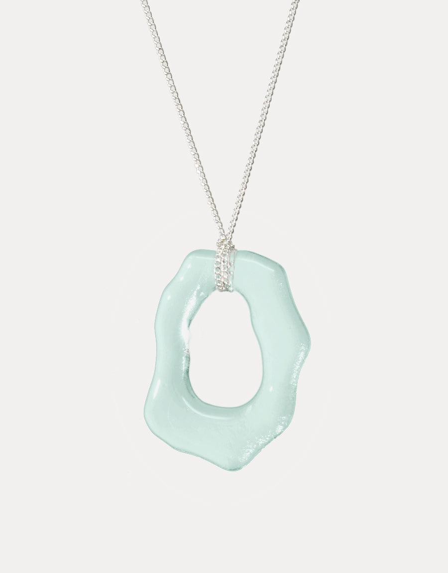 High Tide Necklace featuring a unique, organic-shaped pendant in pale blue recycled glass hanging from a delicate silver chain. Eco-friendly jewelry inspired by ocean waves and coastal elements. Handcrafted sustainable accessory by CLED.
