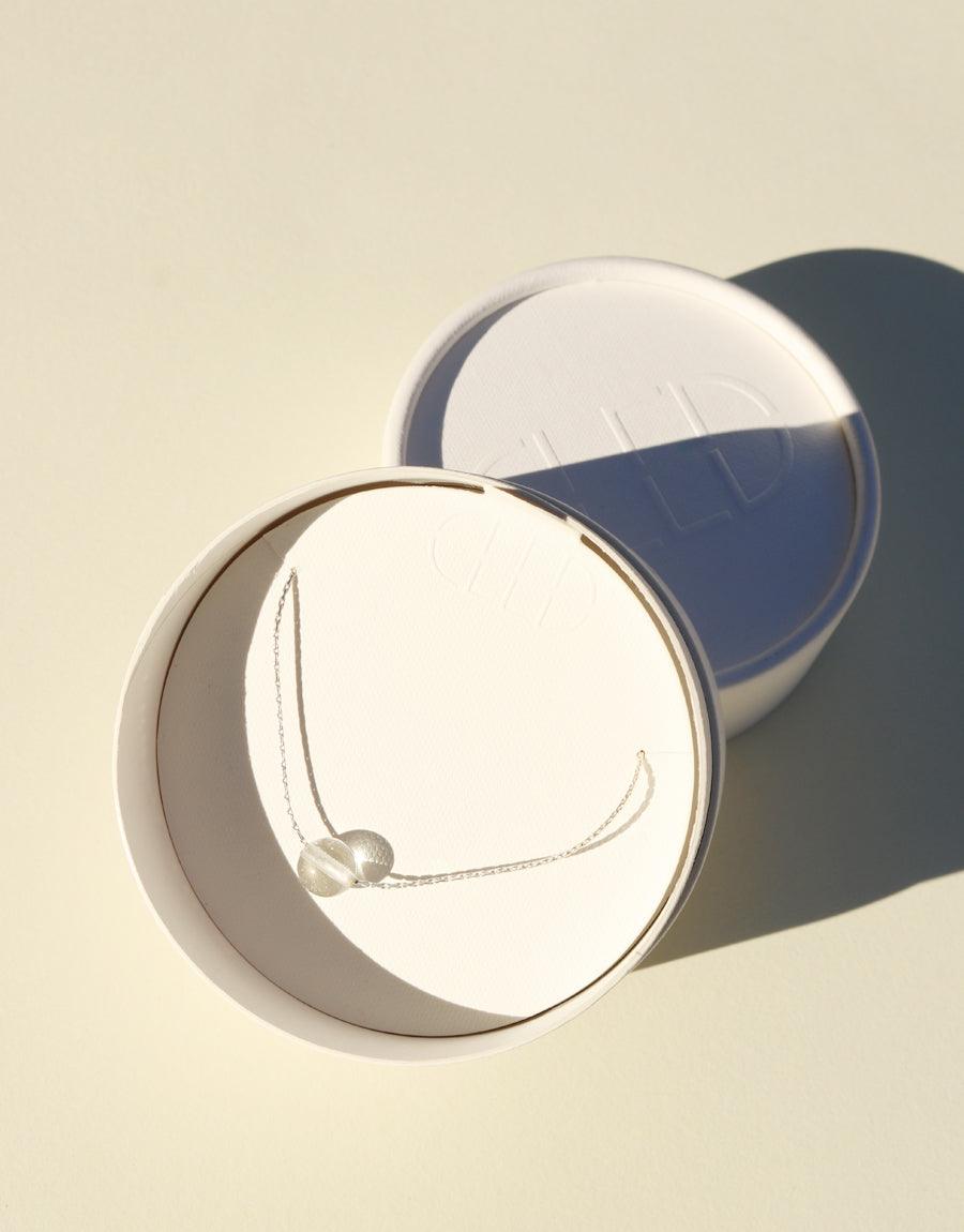 Minimal Ball Necklace showcased in circular white display. Sterling silver chain with delicate Eco Gem pendant, highlighting sustainable elegance. Soft lighting emphasizes the necklace's simplicity and eco-friendly design. Perfect for everyday wear. Handcrafted jewelry by CLED.
