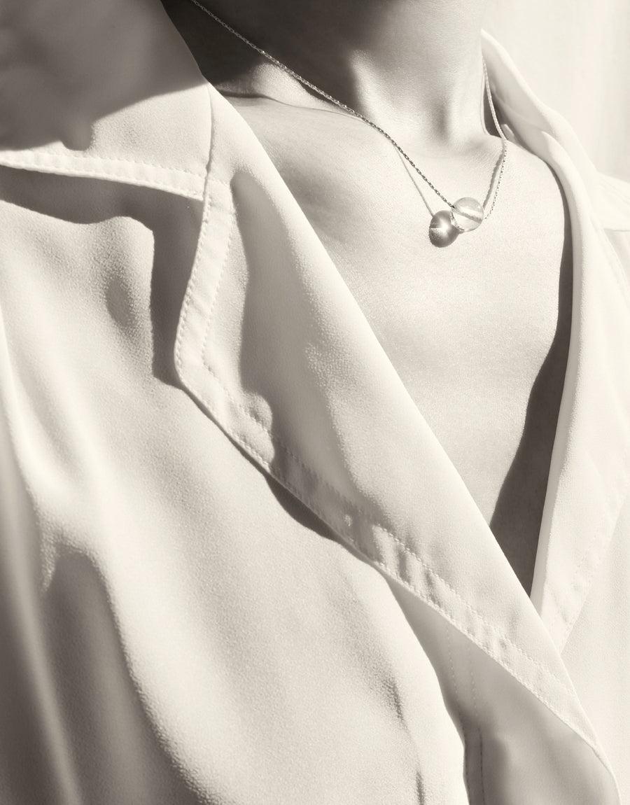 Elegant Minimal Ball Necklace featuring a delicate sterling silver chain and hand-formed glass Eco Gem, worn against a white blouse in a monochrome image showcasing simplicity and sophistication. Sustainable jewelry by CLED.