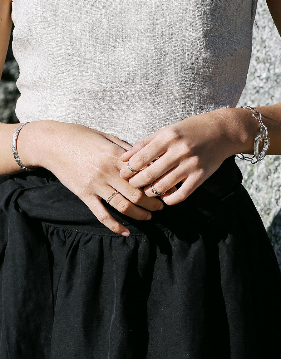 Close-up of hands wearing delicate silver rings, including the Collapsible Chain Ring | C, showcasing versatile styling options for everyday wear. Handcrafted sterling silver jewelry elegantly paired with casual attire, demonstrating the ring's adaptability. CLED