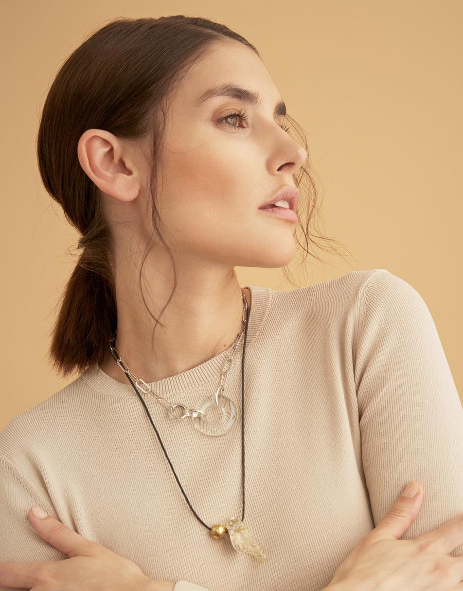 Elegant model showcasing the Opening Necklace, a sterling silver piece with handcrafted glass gems on an oval chain. The necklace complements a neutral-toned outfit, highlighting its versatile and sophisticated design. Made in Los Angeles by CLED.