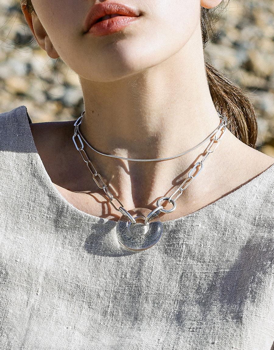 Sterling silver Opening Necklace featuring a handcrafted glass pendant on an oval chain, showcasing sustainable luxury and unique design. Elegant neckline shot highlighting the necklace's distinctive torus gem and eco-friendly craftsmanship. CLED