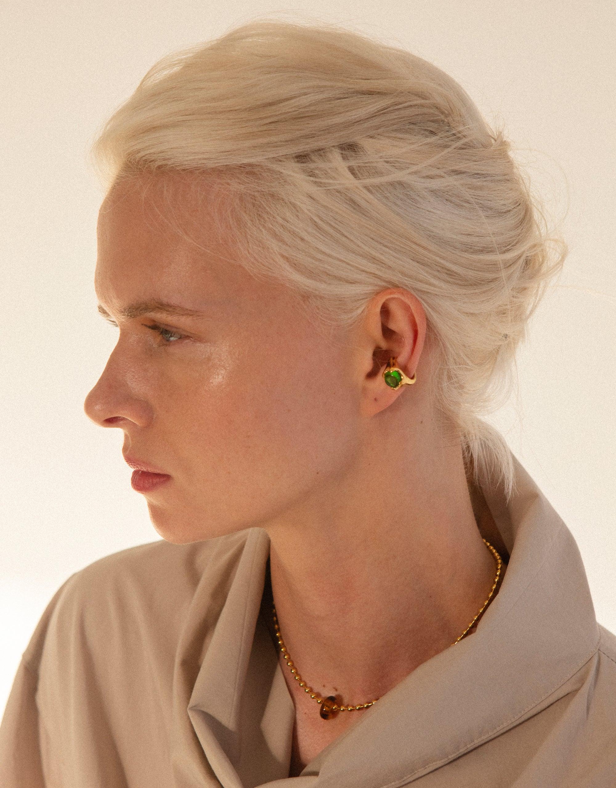 Side profile of a person with platinum blonde hair wearing a beige top and showcasing the Beam Ear Cuff, a vibrant green eco-gem ear accessory that catches the light brilliantly, demonstrating the prism-like effect of CLED's sustainable jewelry design.