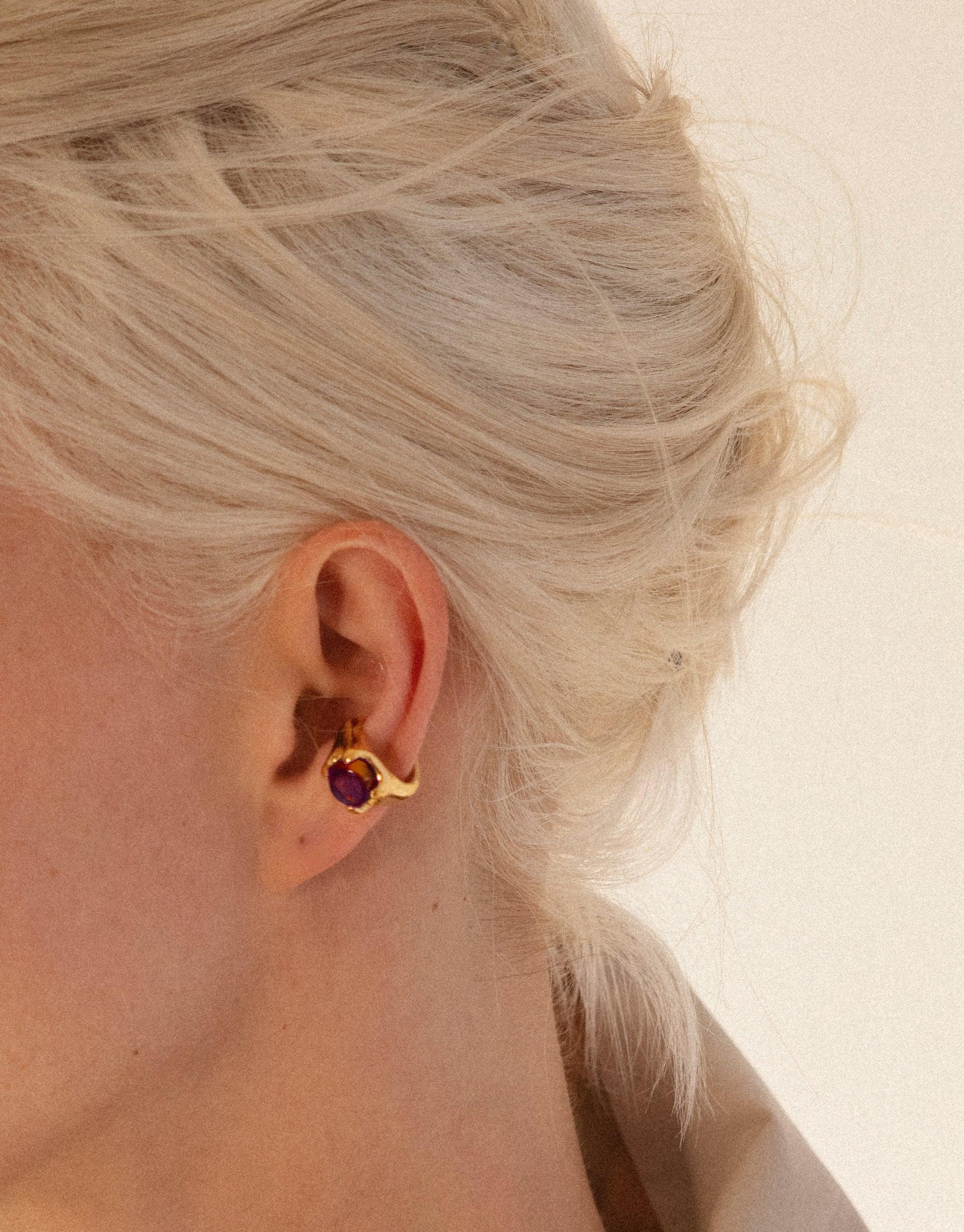 Closeup of blonde hair and ear wearing gold Beam Ear Cuff with purple eco gem, showcasing unique design and sustainable jewelry craftsmanship by CLED