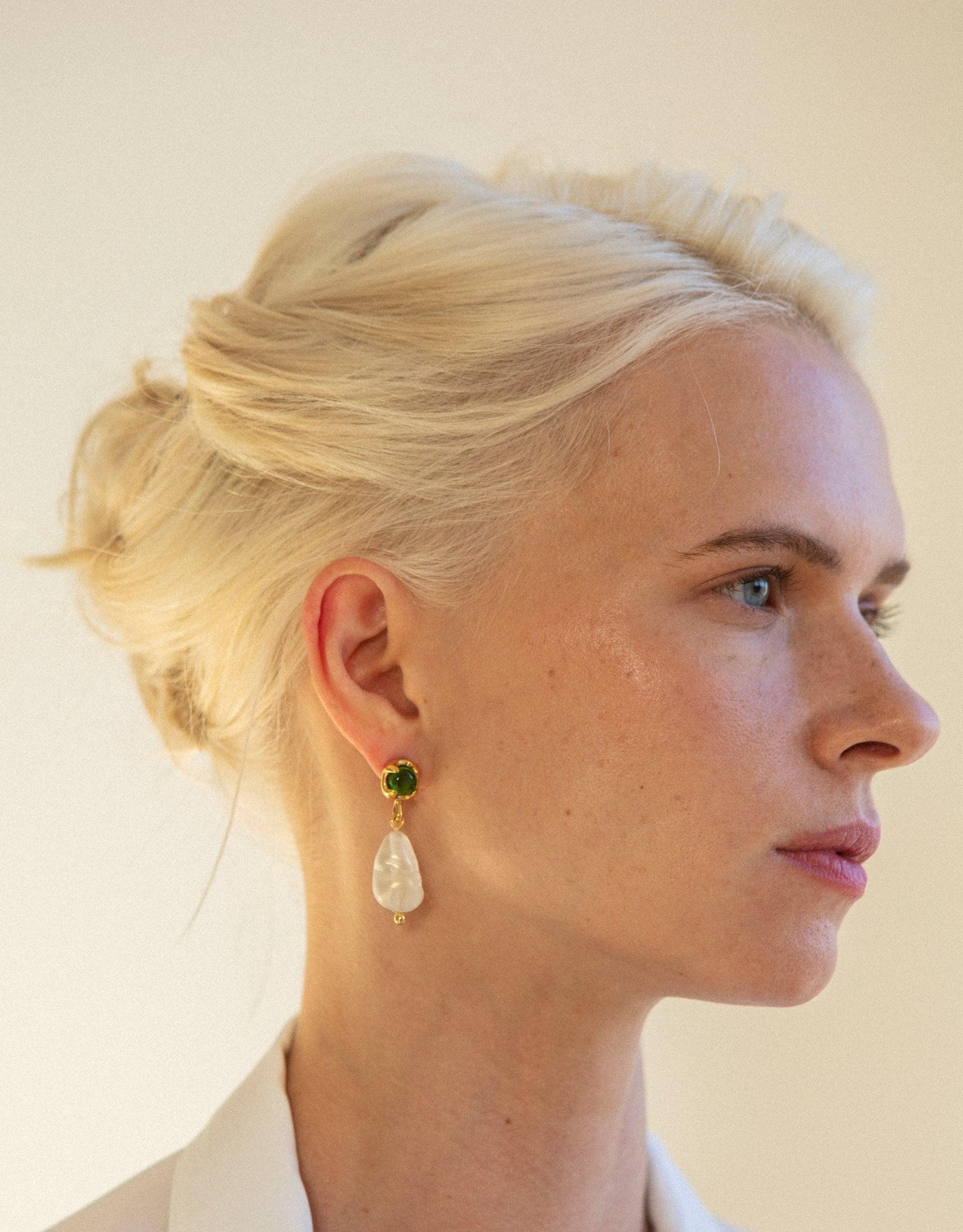 Elegant profile view showcasing Beam Pearl Earrings, featuring a gold-plated drop design with a green gem stud and iridescent pearl-like pendant. Sleek updo hairstyle complements the earrings' refined aesthetic. Sustainable jewelry by CLED.