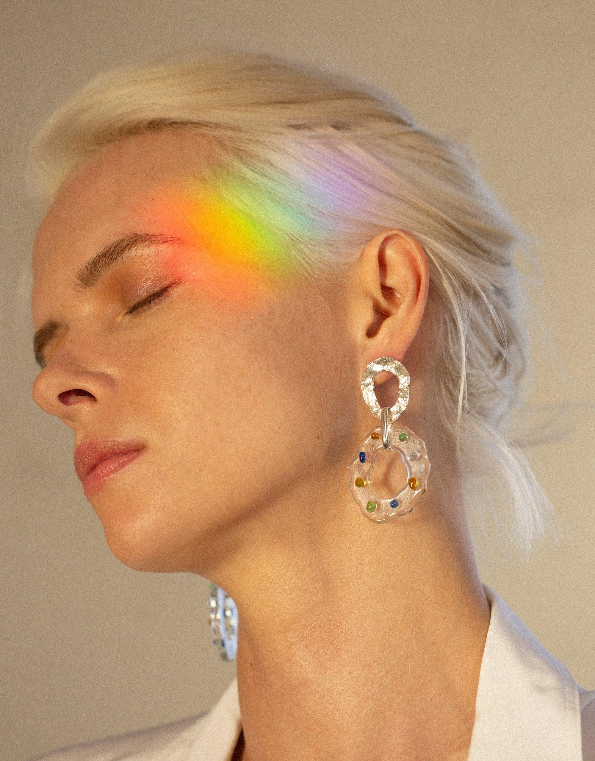 Iridescent rainbow light effect on model wearing High Tide Earrings in Spectrum, featuring circular eco gem design with colorful accents. Handcrafted sustainable jewelry showcasing prismatic colors. CLED High Tide Earrings in Spectrum.