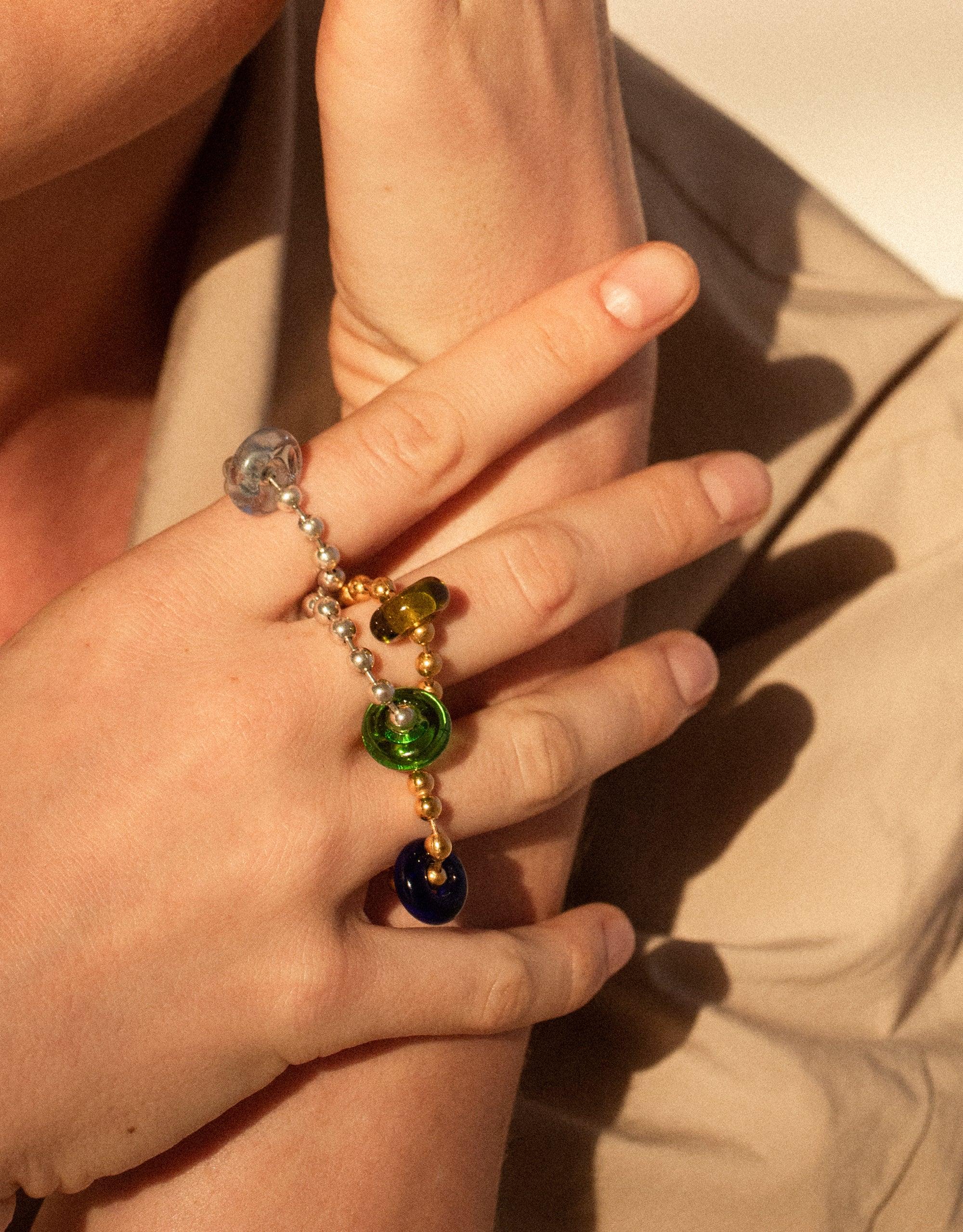 Hand wearing Donut Ball Ring with colorful eco gems in various hues, showcasing prismatic effect of repurposed glass. Unique handmade jewelry piece reflecting sustainability and artistry. Donut Ball Ring by CLED