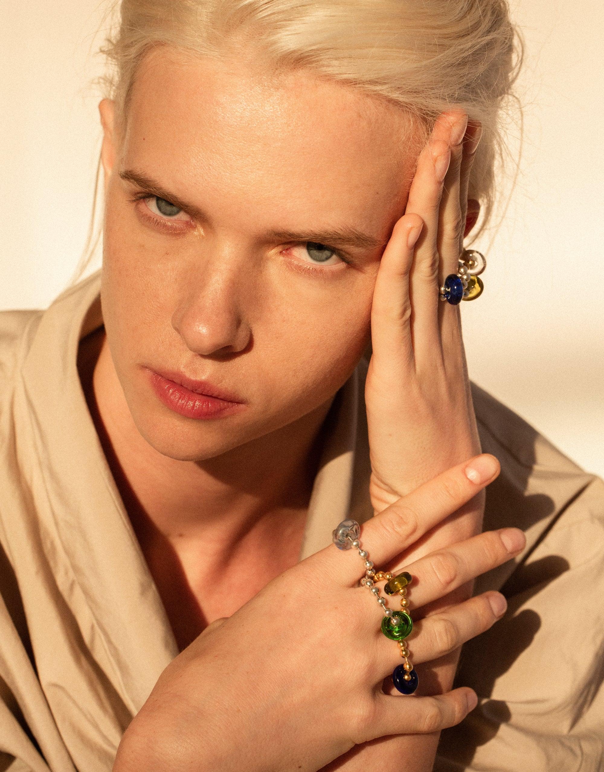 Stylish model wearing Donut Ball Ring with colorful eco gems, showcasing prismatic effect of upcycled glass jewelry. Hand positioned to highlight ring's unique design and sustainable materials. Elegant and eco-conscious accessory by CLED.