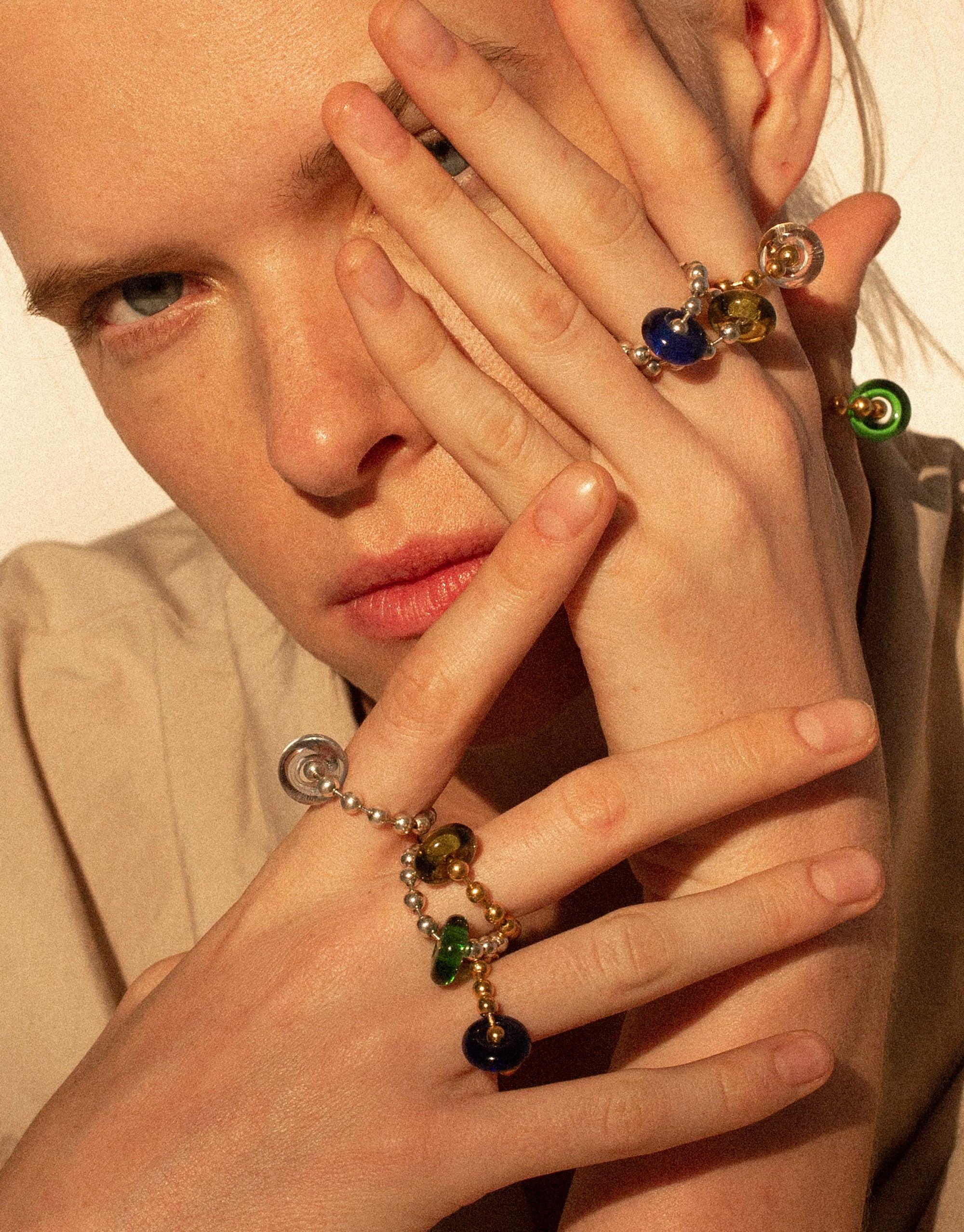 Close-up of hands adorned with colorful glass bead rings, showcasing the Donut Ball Ring collection. Vibrant eco gems in various hues catch the light, demonstrating the prism-like effect. Handcrafted jewelry by CLED featuring upcycled glass in a sustainable design. Donut Ball Ring by CLED.