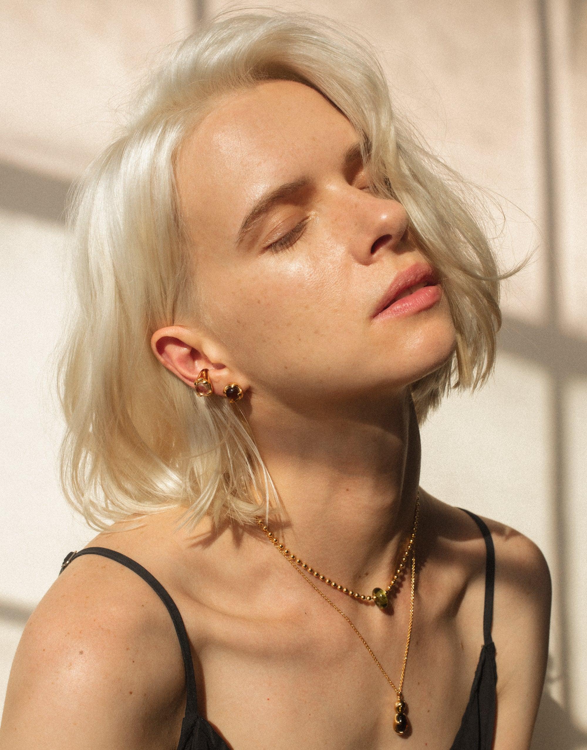 Sunlit portrait showcasing delicate gold Donut Ball Necklace, highlighting eco-friendly jewelry design. Elegant accessory complementing natural beauty and sustainable fashion. Handcrafted CLED eco gem pendant capturing prismatic light effects.