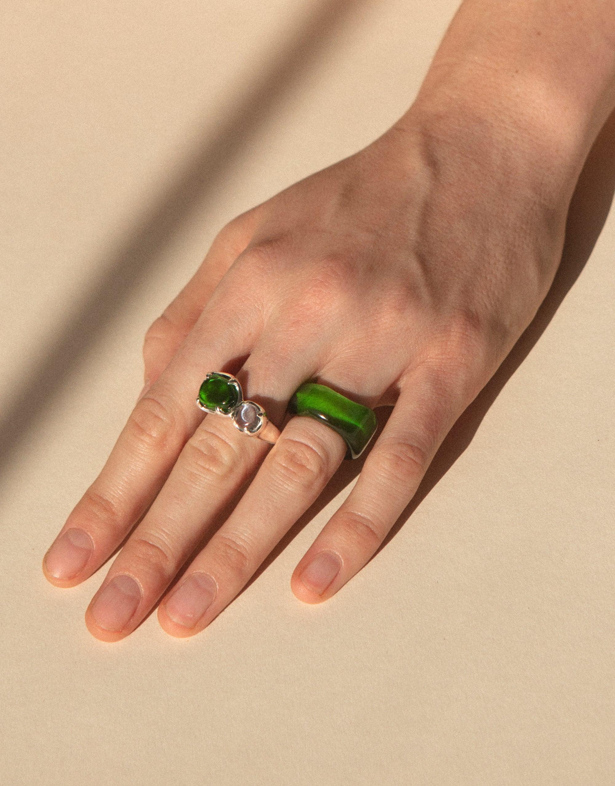 Hand wearing Duo Beam Ring with vibrant green eco gem, showcasing sustainable luxury jewelry. Unique design captures light like a prism, reflecting spectral colors. Handcrafted in Los Angeles using upcycled glass. CLED