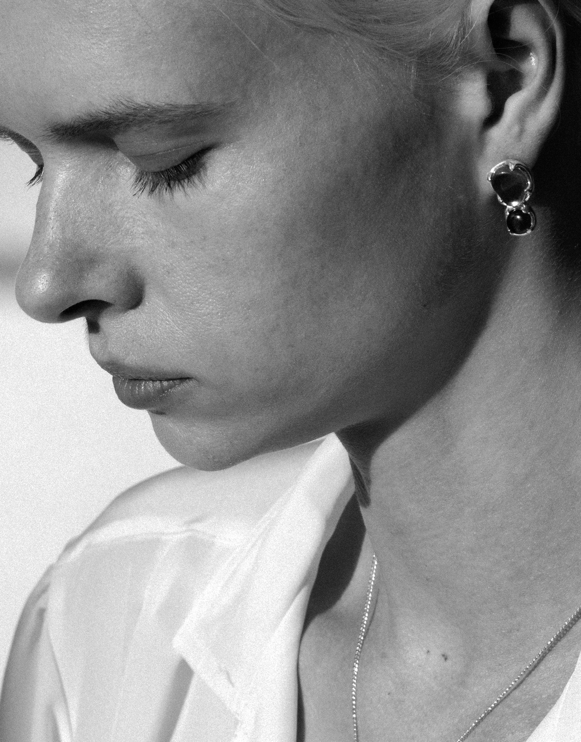 Close-up black and white profile of a person wearing Duo Beam Earrings, showcasing the elegant design and luxurious appeal of the eco-friendly jewelry. The earrings feature a unique shape that catches light, embodying the prism-inspired concept by CLED.