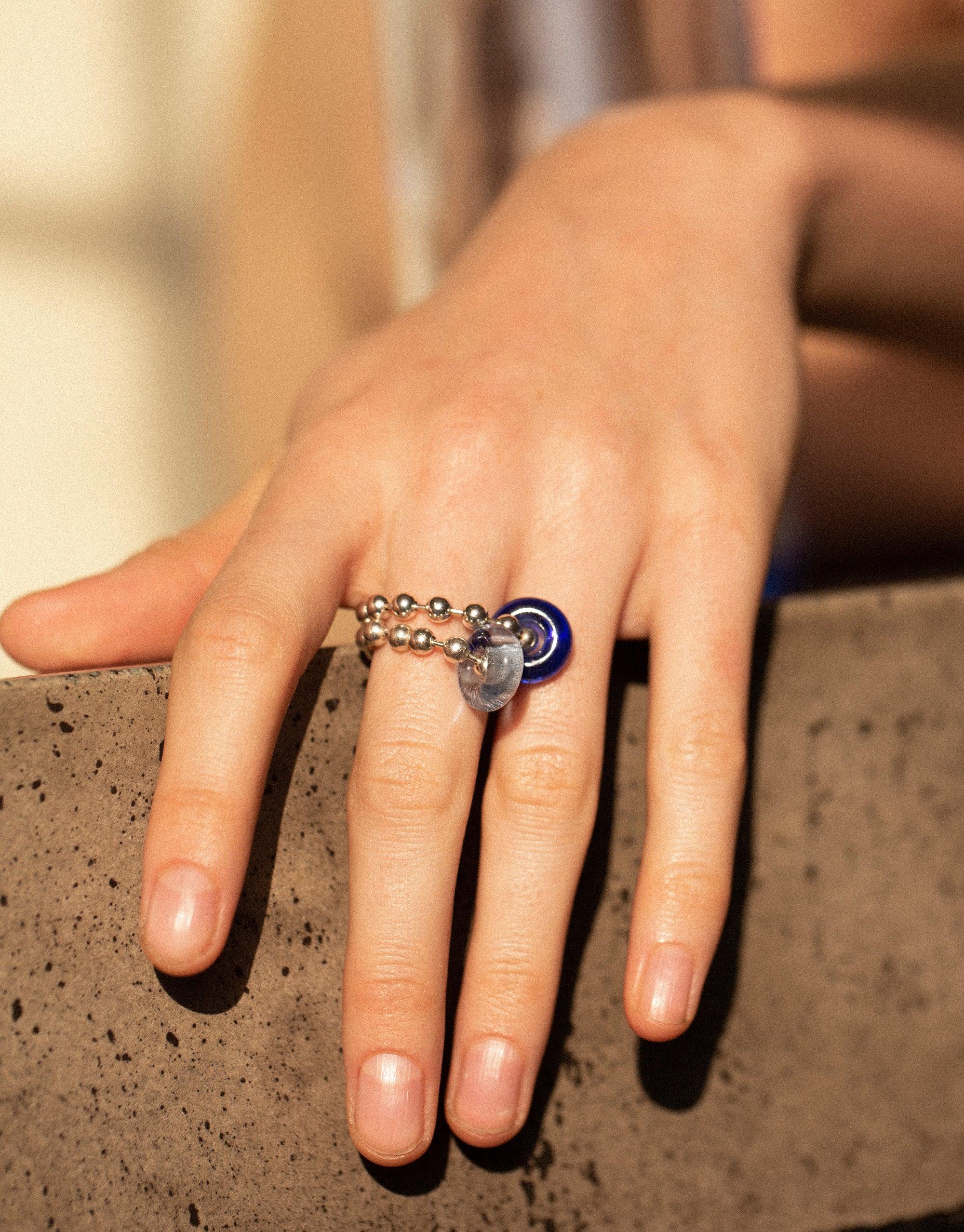 Close-up of hand wearing unique Donut Ball Ring with blue eco gem, showcasing intricate design and sustainable craftsmanship. Sterling silver or gold-plated brass ring with upcycled glass, representing prism-like colors. Handmade in Los Angeles by CLED.