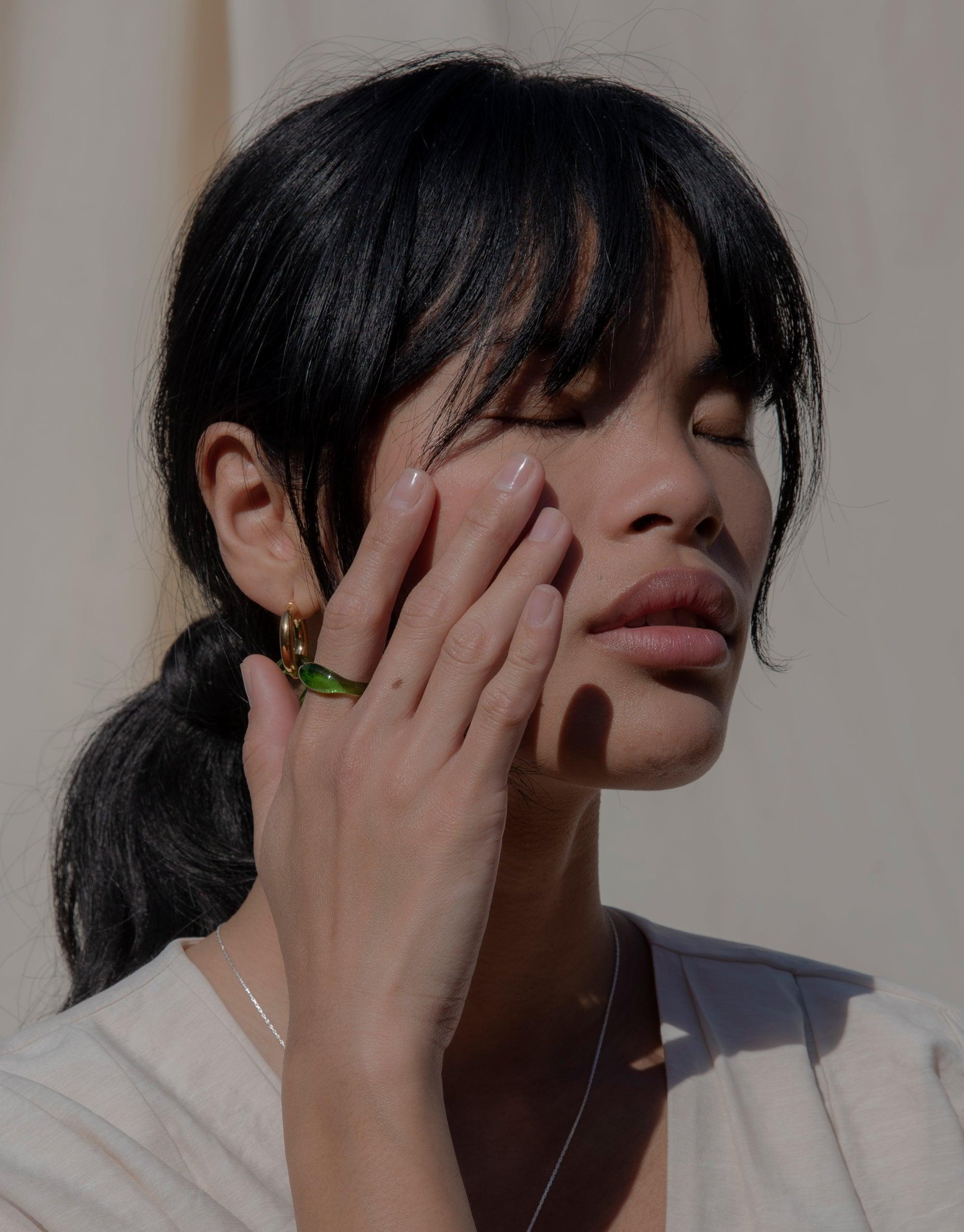 Close-up of a person wearing a green Signet Ring Original, showcasing the eco-friendly jewelry piece from the Messenger Collection. The ring's vibrant color contrasts with the model's hand, highlighting its unique design and craftsmanship by CLED.