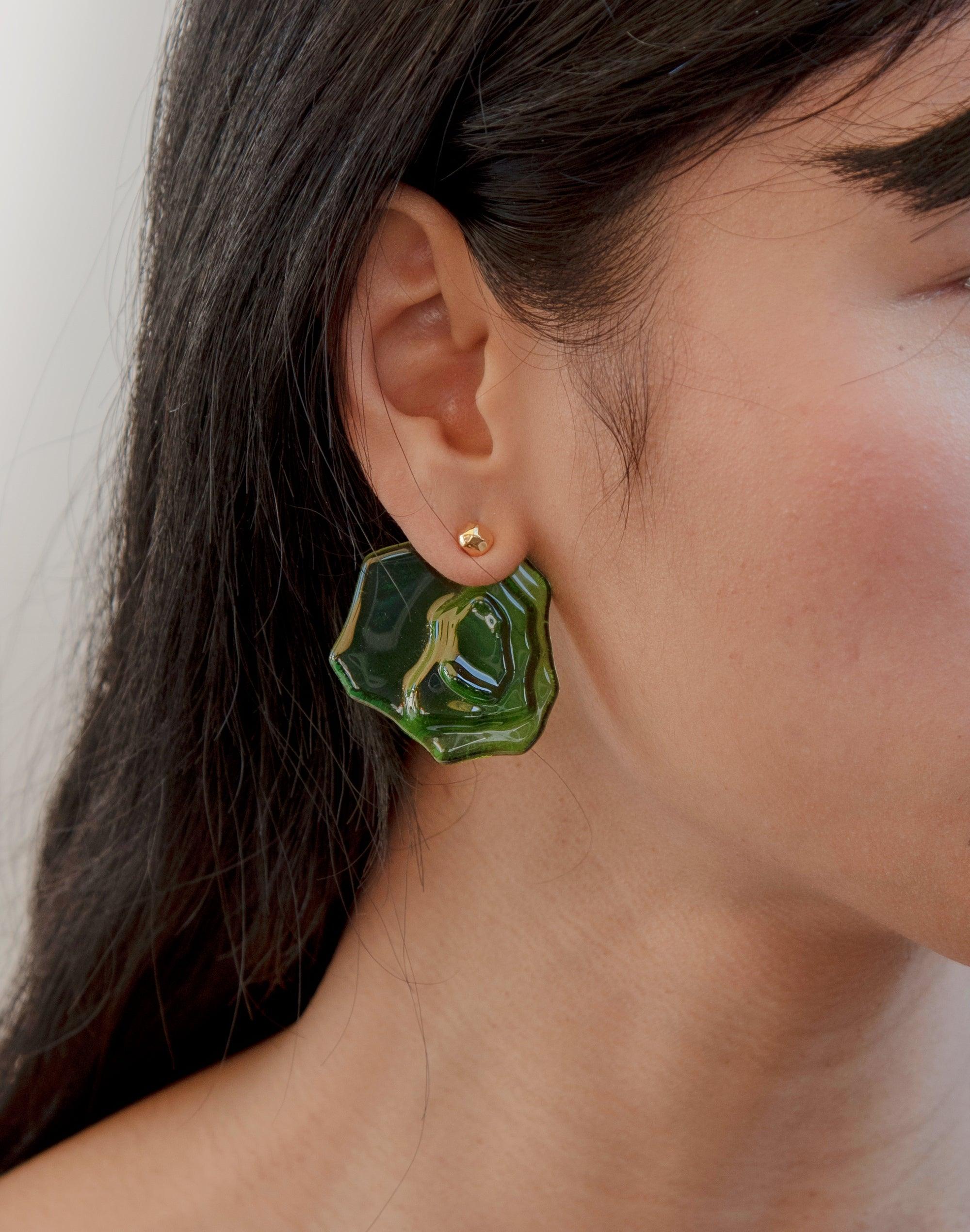 Close-up of a person wearing Plateau Earrings, featuring a unique green glass design inspired by canyon terrain. The earring showcases an abstract, molten form with layered glass, highlighting the eco-friendly and handcrafted nature of CLED's Plateau Earrings.