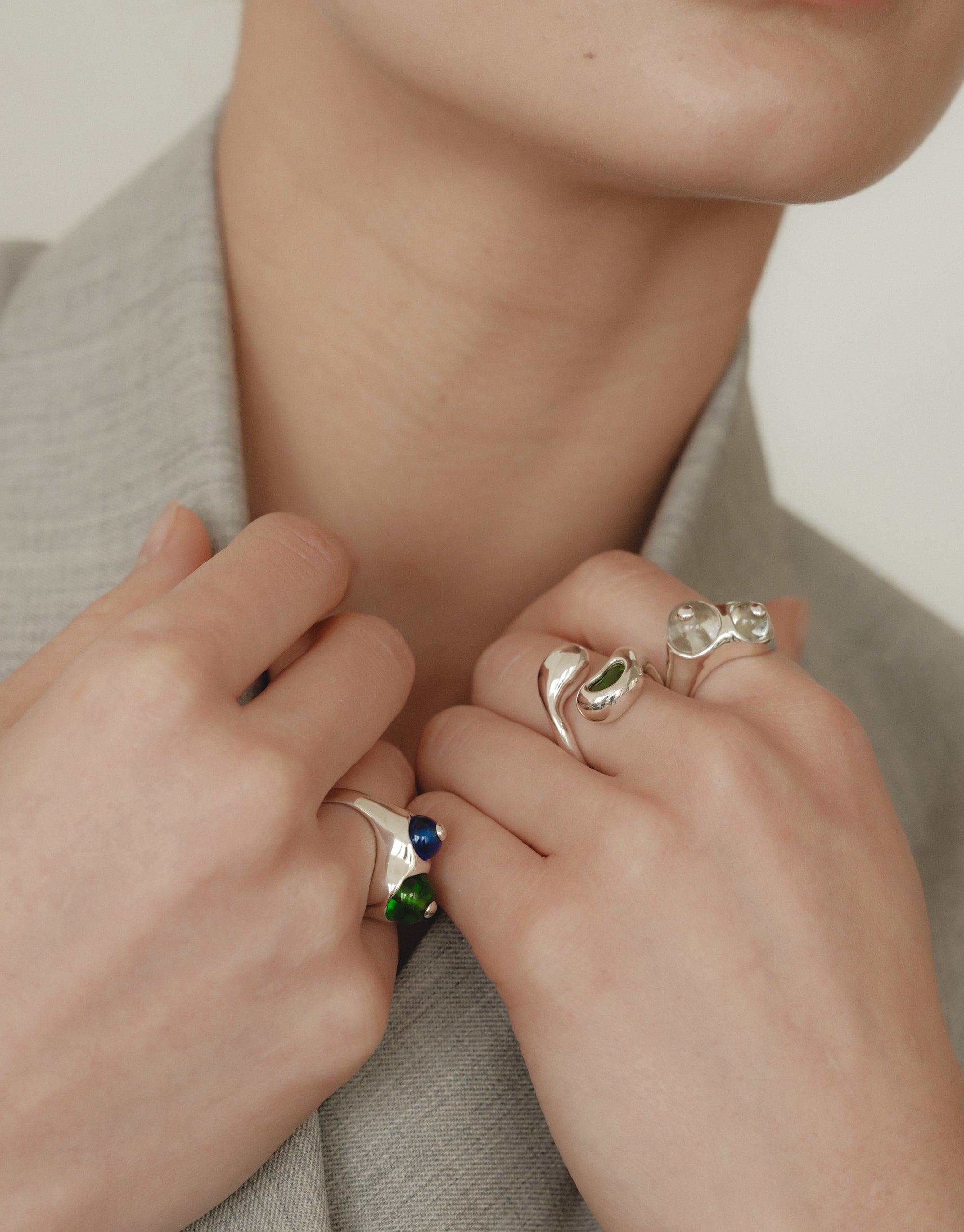 Close-up of hands wearing unique Pod Rings inspired by organic legume shapes, featuring silver designs with colorful accents. The rings showcase nature-inspired curves and patterns, embodying growth and transformation. Elegant jewelry piece from the CLED collection.