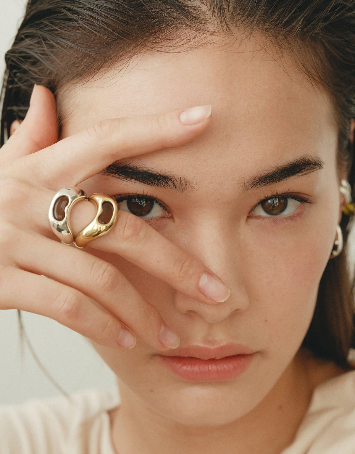 Close-up of a model wearing the Bean Ring, showcasing its unique organic shape inspired by legume plants. The ring's curved design elegantly frames the model's eye, highlighting the jewelry's natural beauty and transformative energy. Bean Ring by CLED.