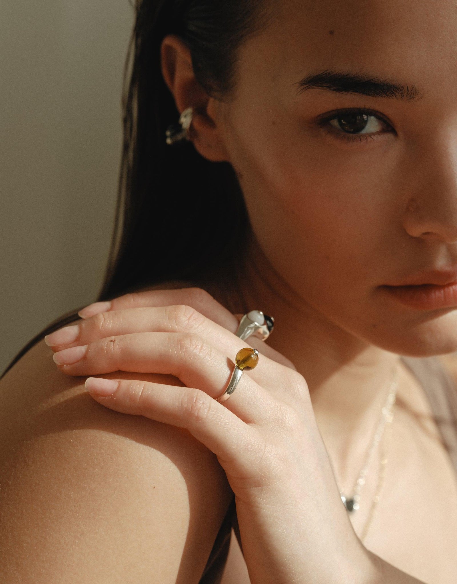 Close-up of a hand wearing the Pea Curve Ring | Large, showcasing its organic shape inspired by legumes. The silver ring features a unique curved design with a yellow accent, capturing nature's creativity. Elegant jewelry piece reflecting growth and transformation. CLED