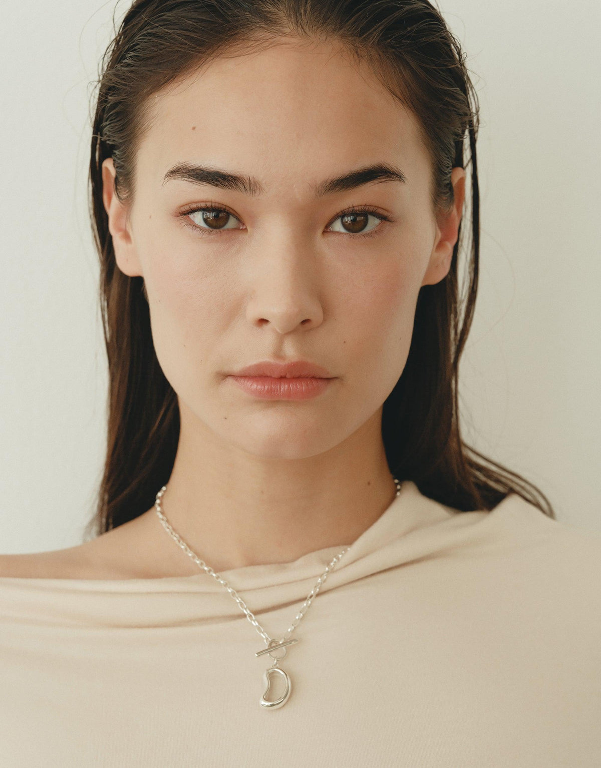 Elegant model wearing Bean Toggle Necklace, showcasing nature-inspired design with organic shapes. Delicate silver chain and bean-shaped toggle pendant, reflecting growth and transformation. Perfect accessory for a sophisticated, natural look. Bean Toggle Necklace by CLED