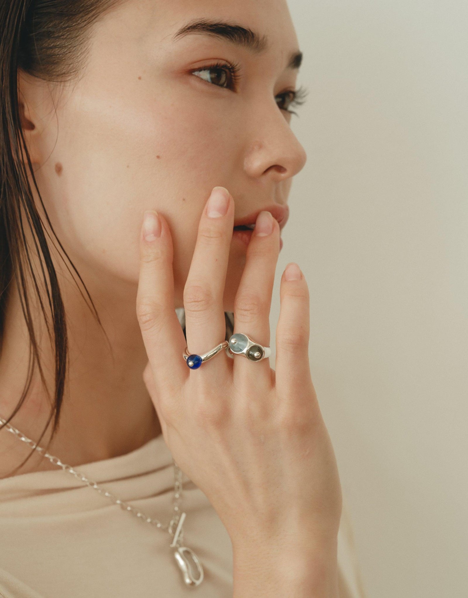Close-up of a hand touching a face, showcasing a unique silver ring with an organic, curved design inspired by nature. The ring's shape mimics the gentle curves of a legume, embodying growth and transformation. Pea Curve Ring | Large by CLED.