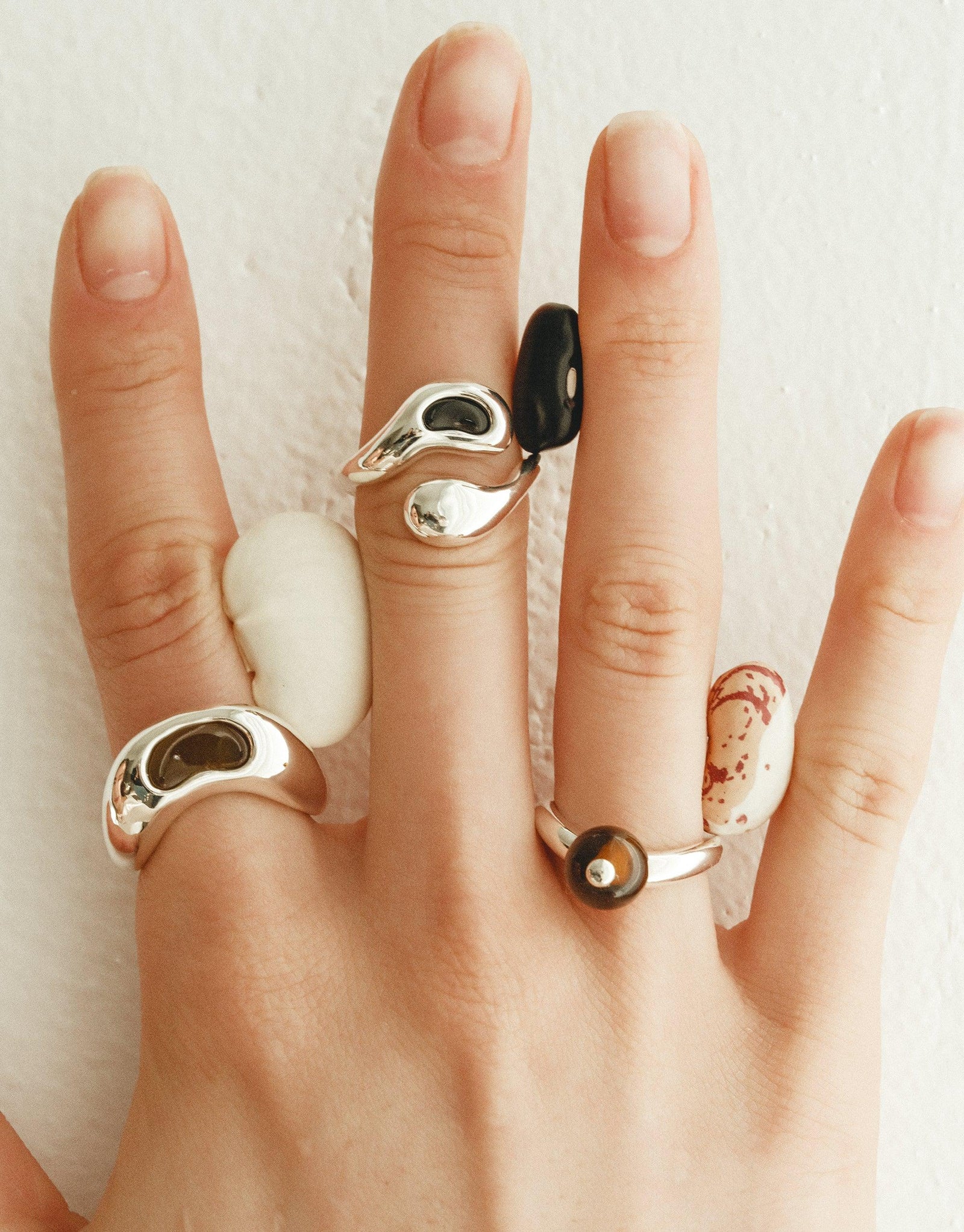 Sculptural silver and organic-shaped rings inspired by legumes, showcasing nature's creativity. Bean Ring collection features unique designs with smooth curves and contrasting elements, worn on multiple fingers. Sustainable jewelry capturing the essence of growth and transformation. CLED Bean Ring
