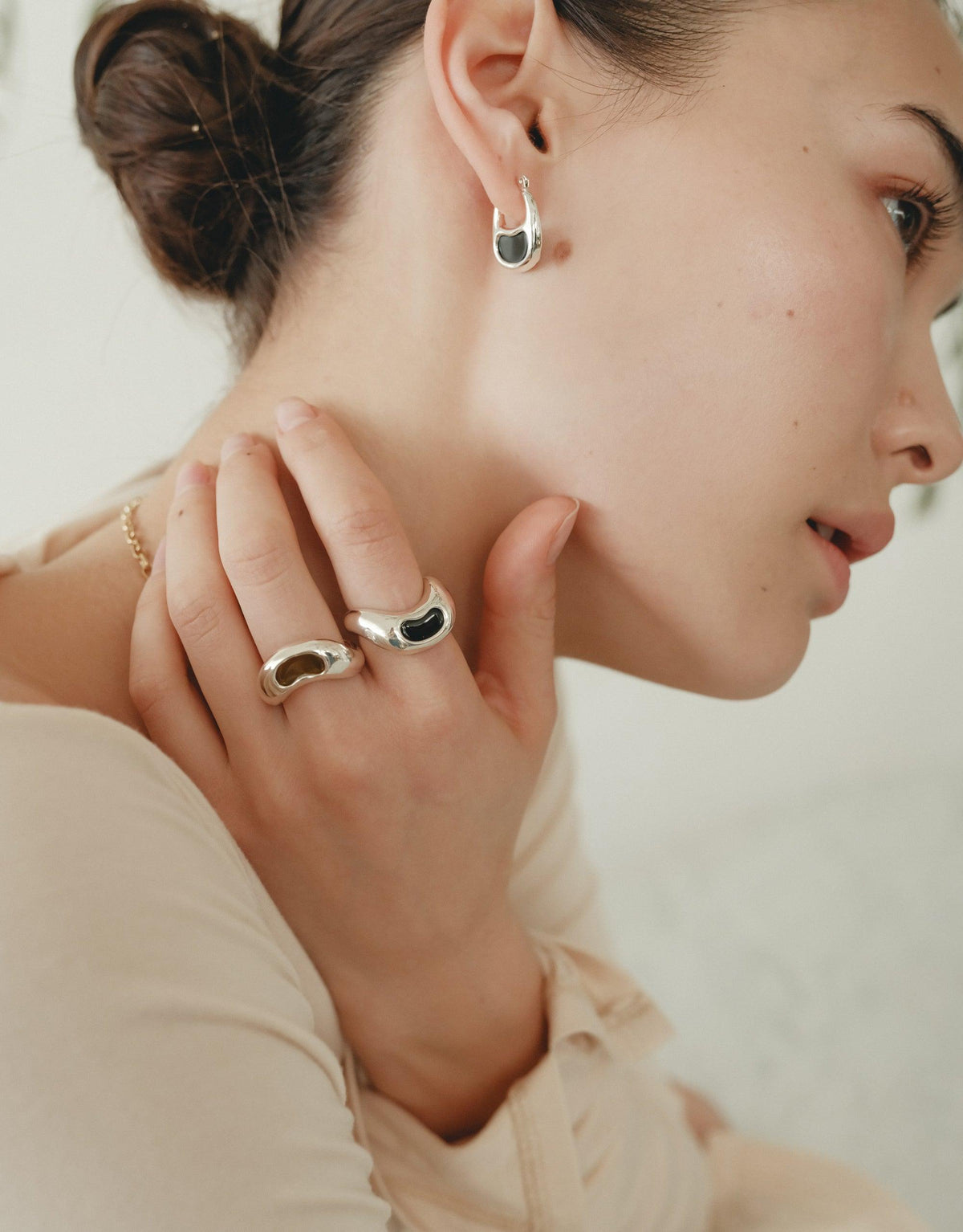 Elegant model showcasing Bean Ring jewelry, featuring organic shapes inspired by legumes. Silver earrings and rings with curved designs, reflecting nature's beauty. Soft profile view emphasizes the delicate and transformative essence of the collection. Bean Ring by CLED