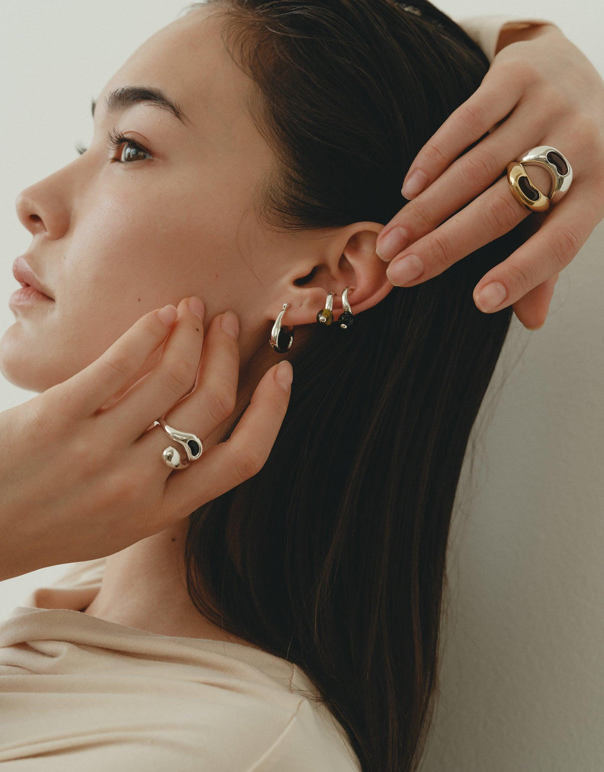 Profile view of a model showcasing multiple earrings and rings, including the Bean Ring inspired by organic shapes and nature's creativity. The jewelry complements the model's elegant profile, emphasizing the collection's unique design. CLED Bean Ring.