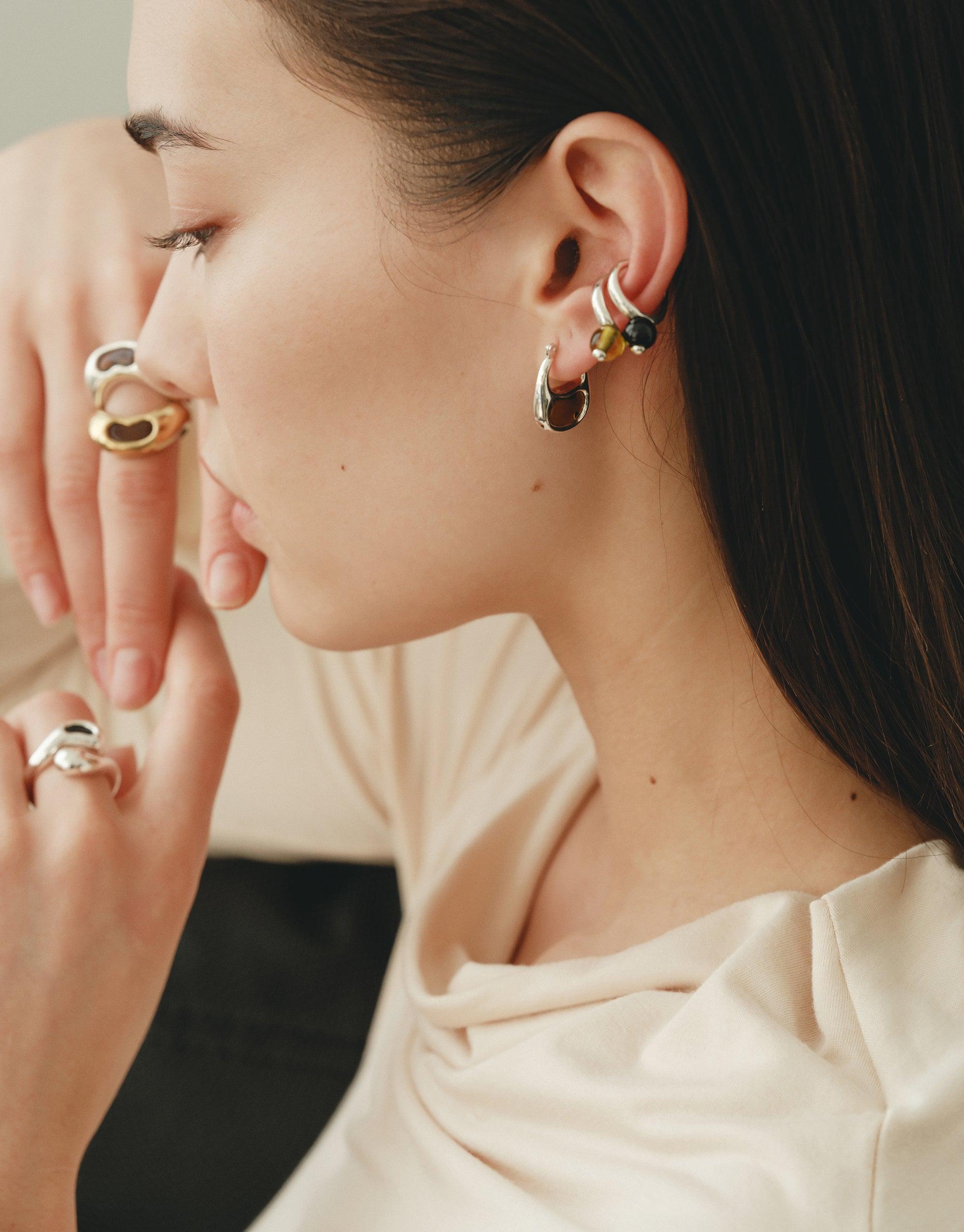 Close-up of a woman wearing small hoop earrings inspired by bean shapes, showcasing the organic design and natural curves. The earrings complement her elegant profile and cream-colored top, embodying growth and transformation. Bean Hoop Earrings | Small by CLED
