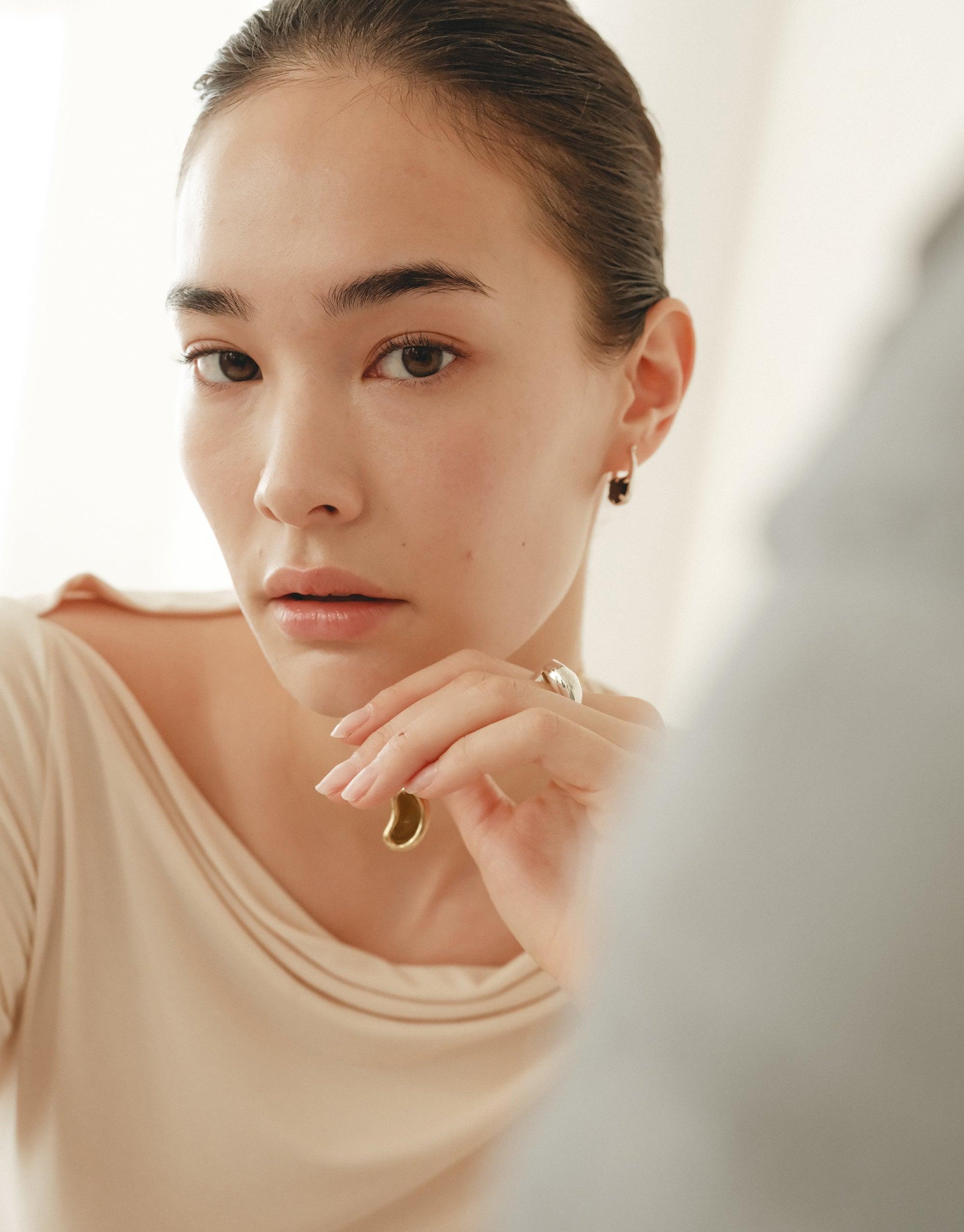 Elegant model showcasing delicate Bean Hoop Earrings, Small, inspired by nature's organic shapes. Soft lighting highlights the earrings' subtle curves, capturing the essence of growth and transformation. Perfect accessory for a sophisticated, nature-inspired look. CLED Bean Hoop Earrings | Small