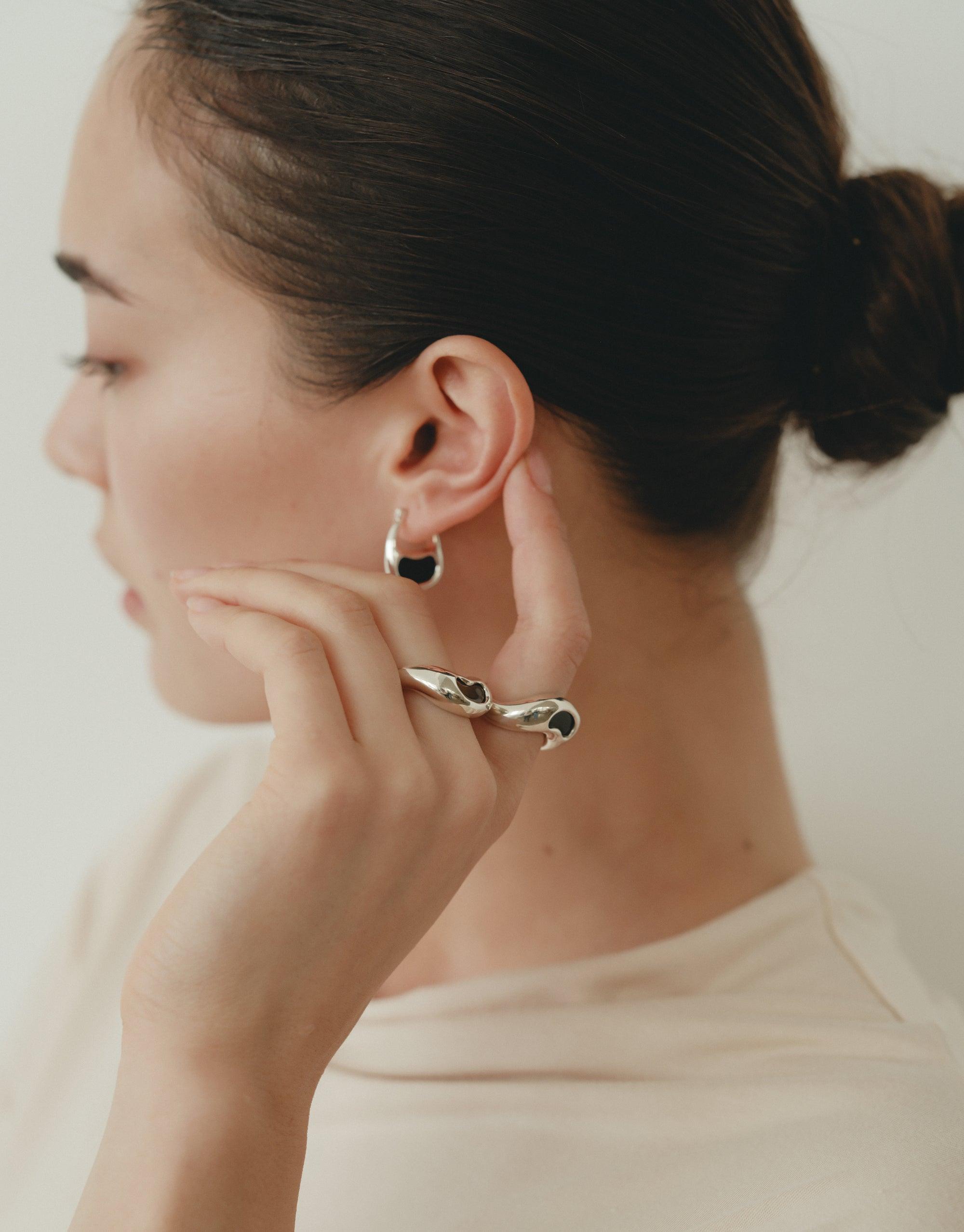 Profile view of a woman wearing small silver hoop earrings with a bean-inspired design, showcasing the Bean Hoop Earrings | Small. Her hand touches her face, highlighting the elegant and nature-inspired jewelry. CLED