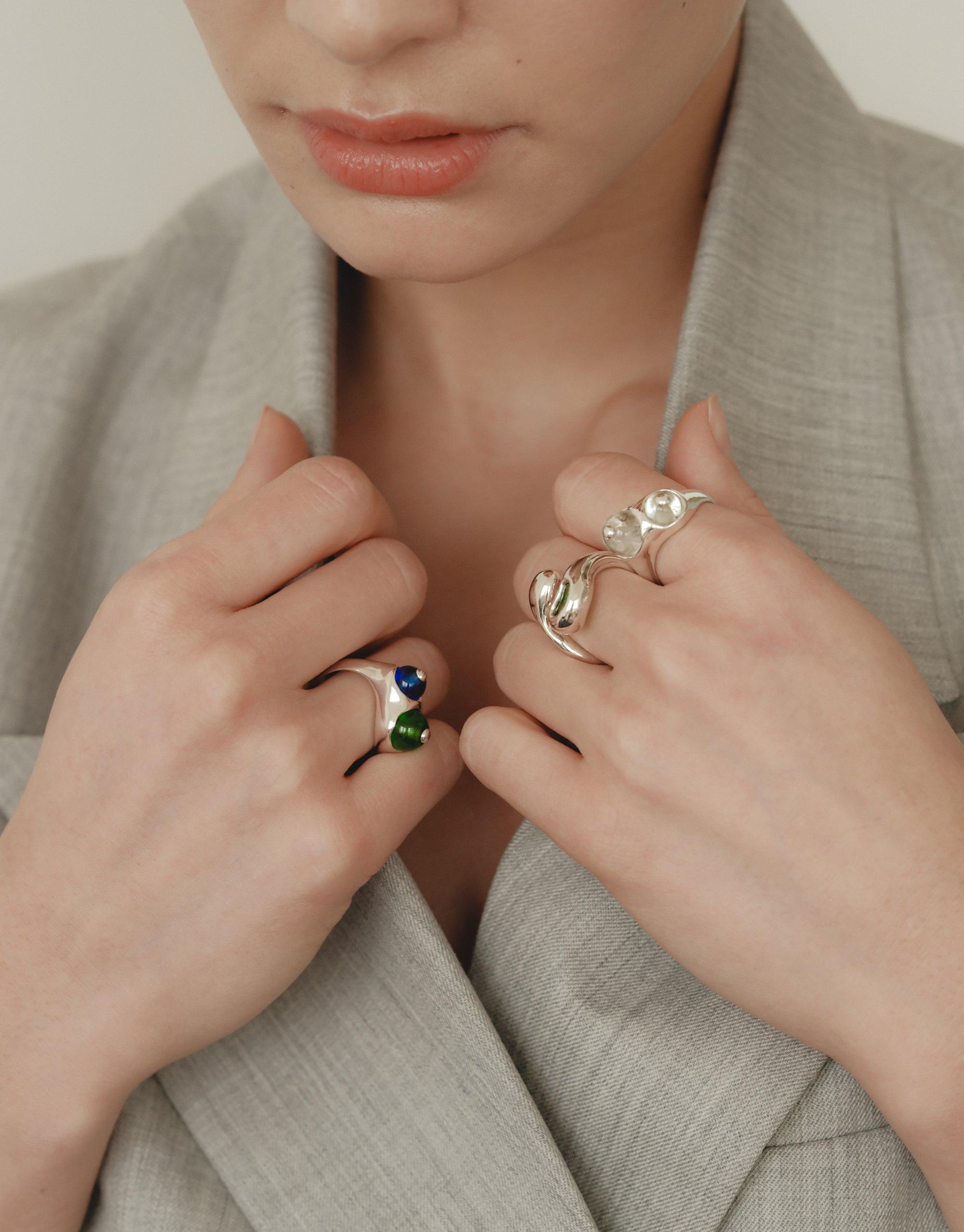 Close-up of hands wearing unique silver rings inspired by organic shapes, including the Pod Ring with its naturalistic design. The rings showcase the beauty of nature-inspired jewelry against a neutral background. CLED Pod Ring.