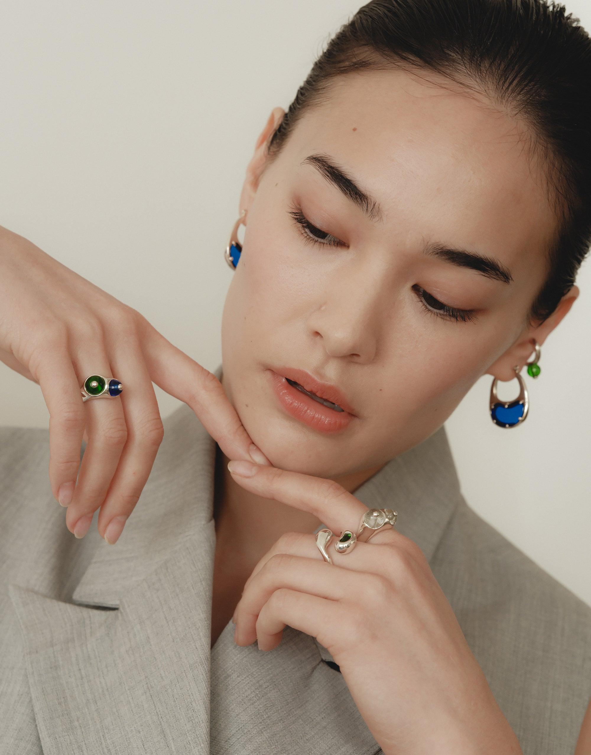Close-up of a model wearing nature-inspired jewelry, including a unique Pod Ring and earrings. The jewelry showcases organic shapes and vibrant colors, reflecting the beauty of legumes and natural patterns. Elegant and transformative design by CLED.