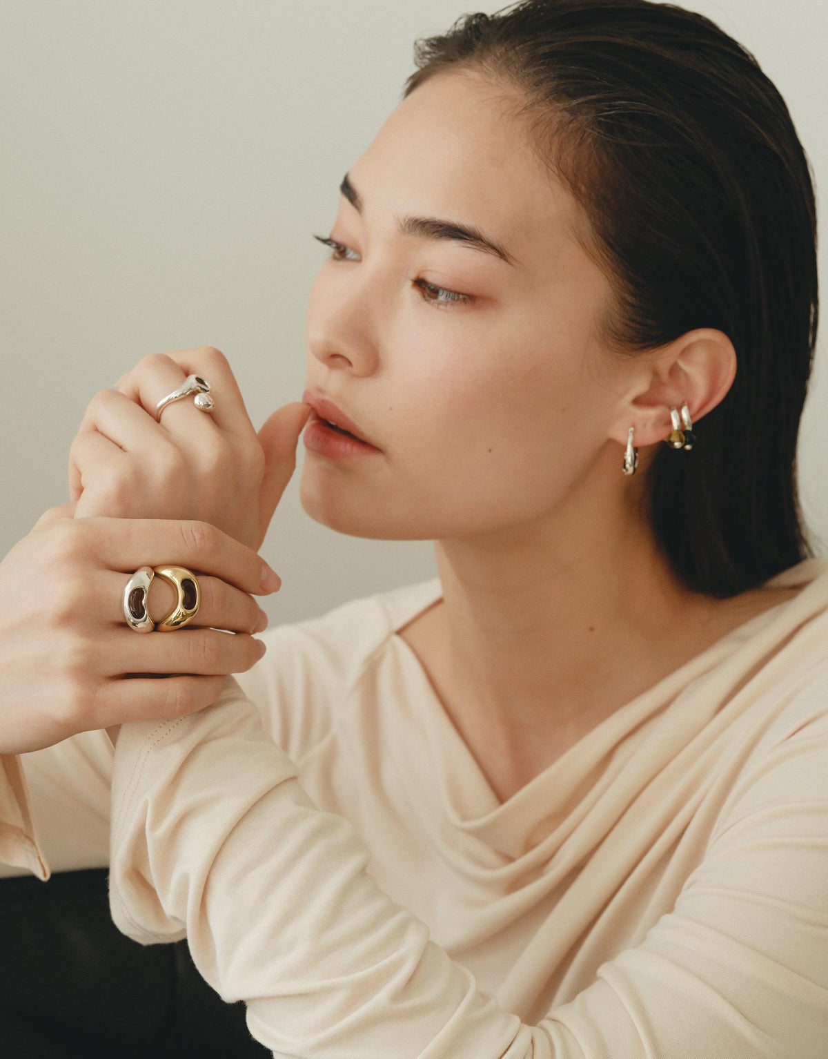 Elegant model showcasing small hoop earrings inspired by organic bean shapes, complemented by stylish rings. Nature-inspired jewelry that captures the essence of growth and transformation. by CLED