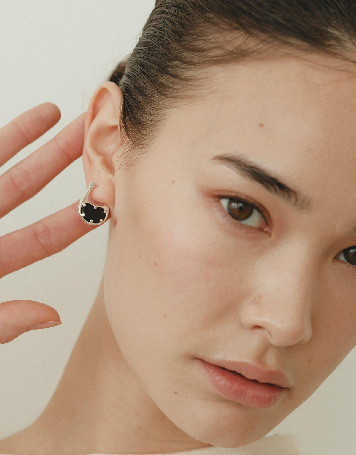 Close-up of model wearing small bean-shaped hoop earrings, showcasing the elegant and nature-inspired design. The earrings feature a dark center, contrasting with the silver metallic outline, highlighting the organic shape inspired by legumes. Bean Hoop Earrings | Small by CLED