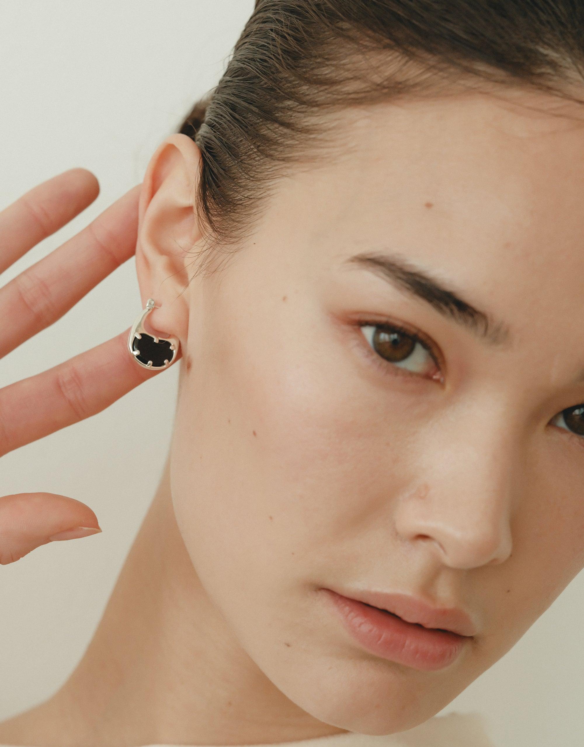 Close-up of model wearing small bean-shaped hoop earrings, showcasing the elegant and nature-inspired design. The earrings feature a dark center, contrasting with the silver metallic outline, highlighting the organic shape inspired by legumes. Bean Hoop Earrings | Small by CLED