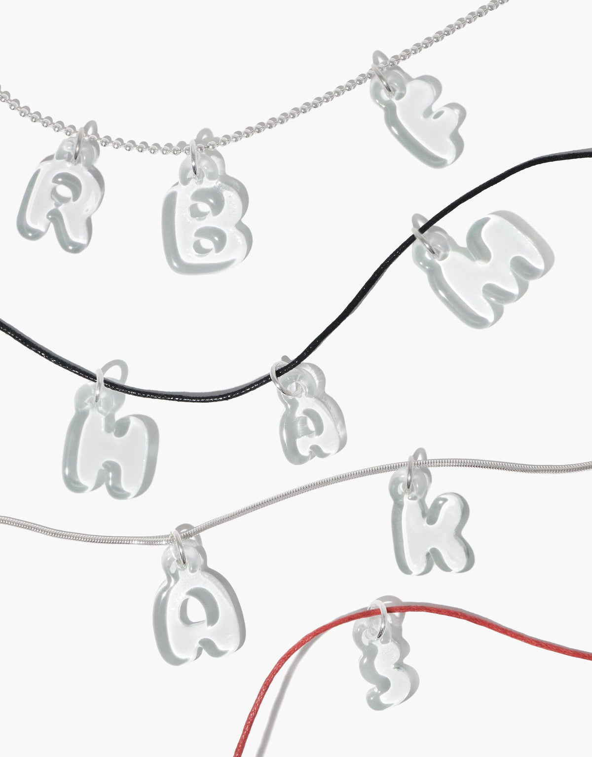 Transparent bubble-style letter charms on various colored necklace chains, showcasing the Letter Charm | Alphabet product. Eco-friendly and playful design made from recycled glass, perfect for personalized jewelry. CLED